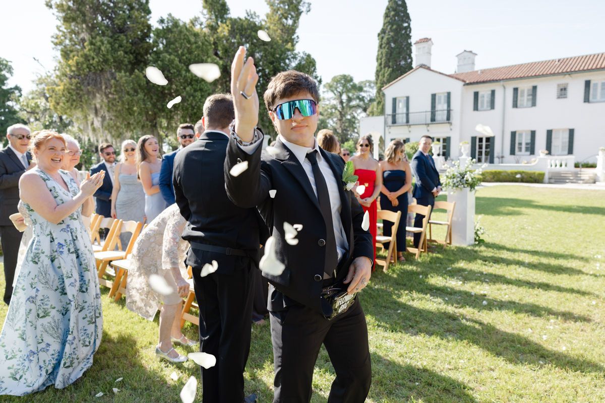Bride’s brother as a flower bro tossing petals at the camera in a funny wedding photo at Crane Cottage Sunken Garden, Jekyll Island Club.