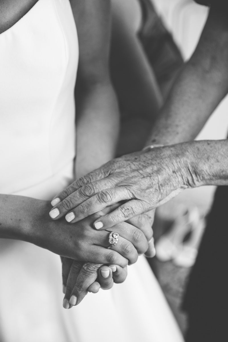 Documentary-style black and white image of sweet moment with bride and mother holding hands, captured by Sea Island wedding photographer.