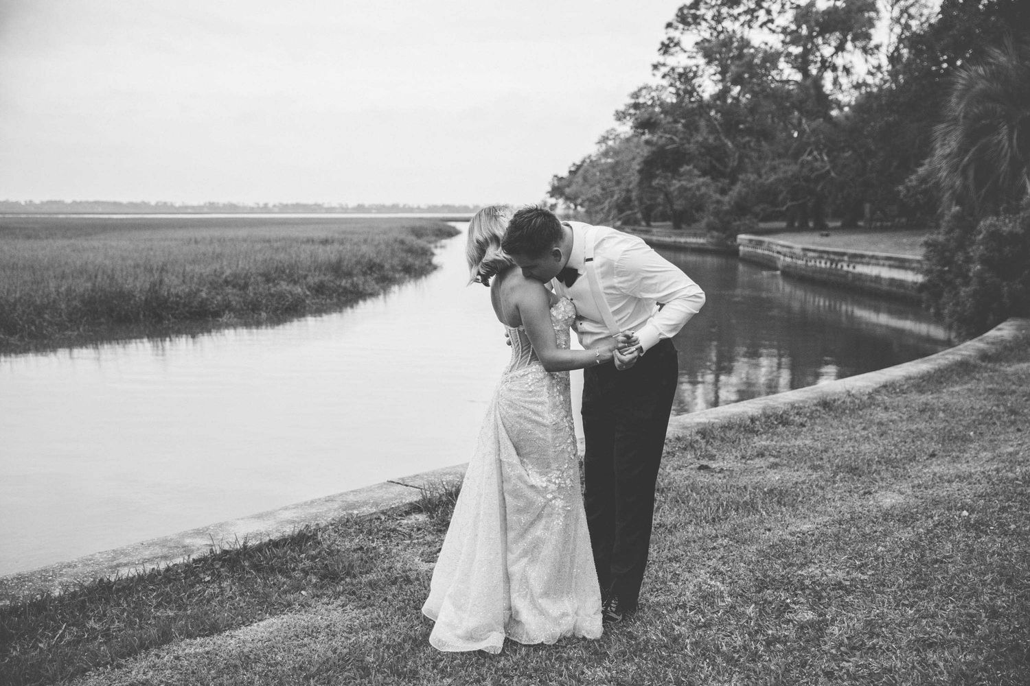 Black-and-white editorial-style wedding photo of a groom kissing bride on St Simons Island with Sea Island marsh behind.