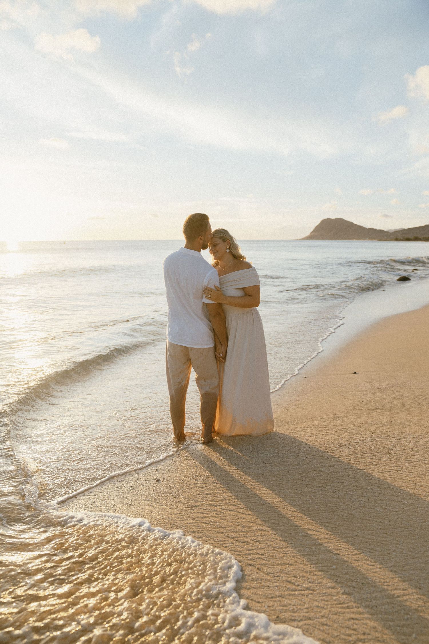 A couple sits together on the beach watching the sunset over the ocean.