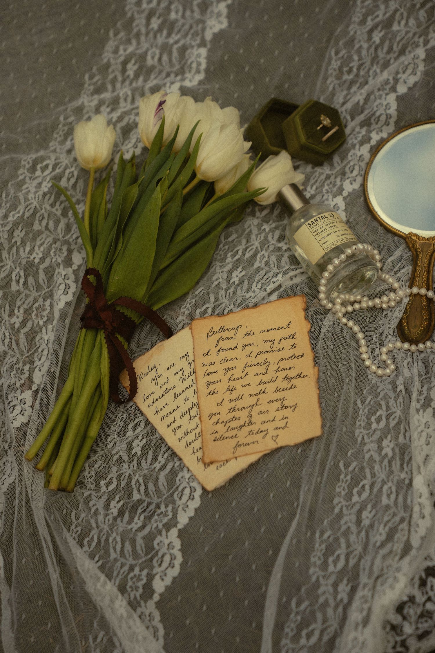 White tulips, handwritten love letters, and pearl necklace arranged on lace fabric.
