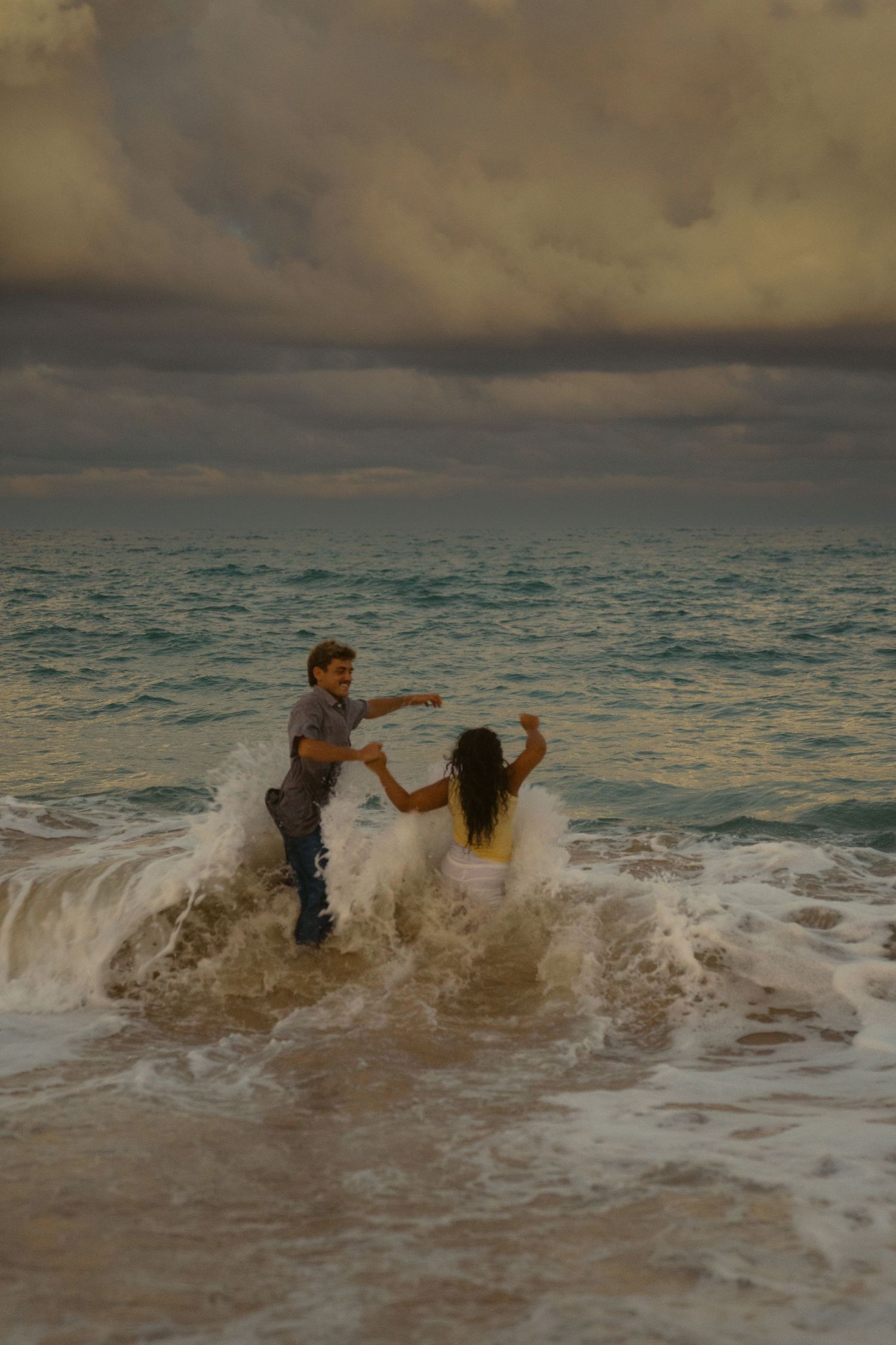 A couple plays in the ocean waves during sunset at a tropical beach.