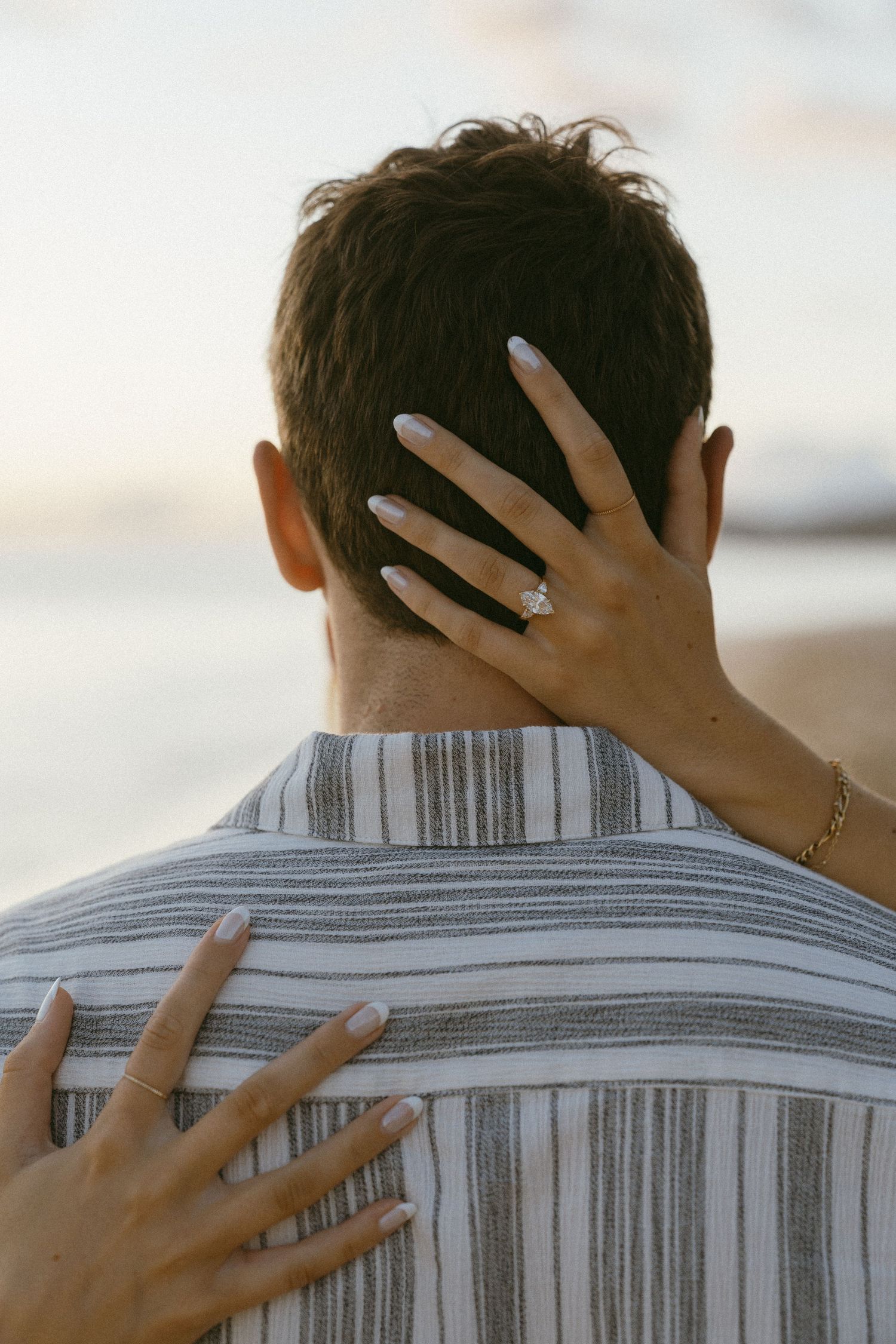 Hands with an engagement ring rest on a striped shirt, showing the special moment.