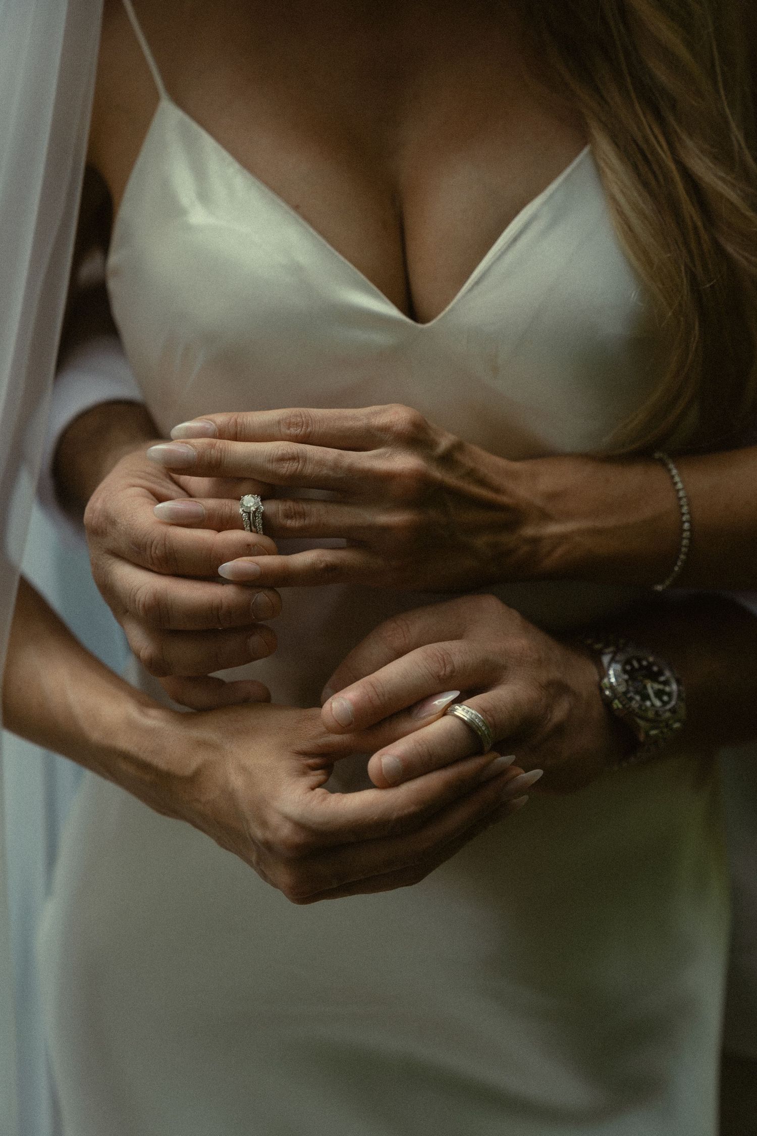 Close-up shot of hands displaying wedding rings and jewelry against a soft background.
