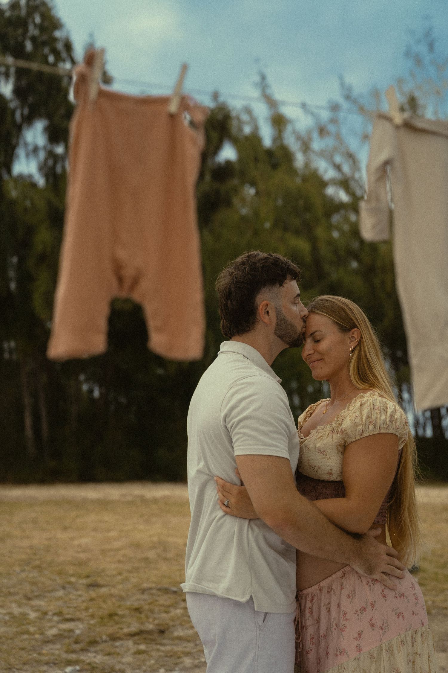 A tender embrace between two people on a beach with vintage clothing hanging nearby.