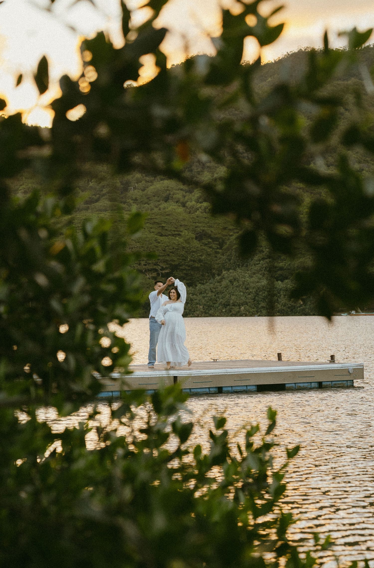 A romantic sunset scene with a couple sitting on a dock surrounded by tropical waters and mountains.