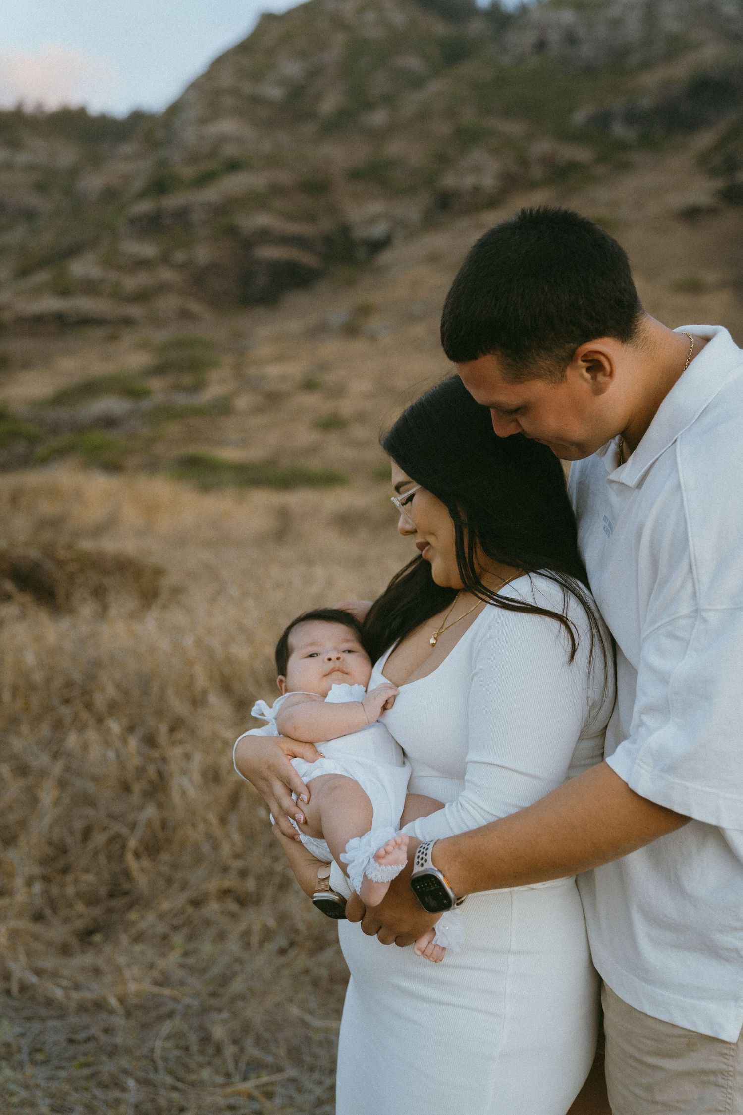 A family shares tender moments outdoors against a natural hillside backdrop.