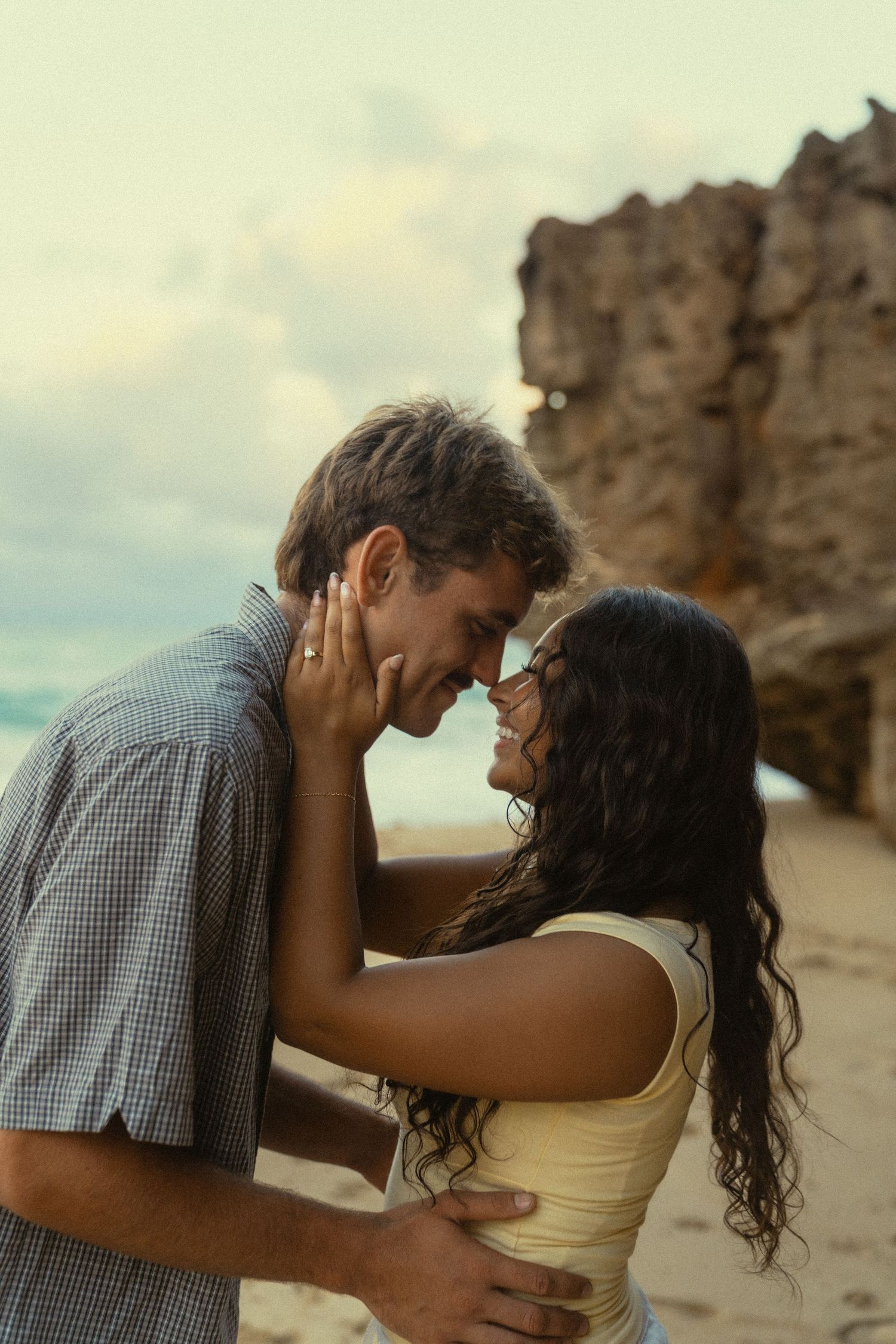 A tender moment shared between a couple on a tropical beach with rocky cliffs.