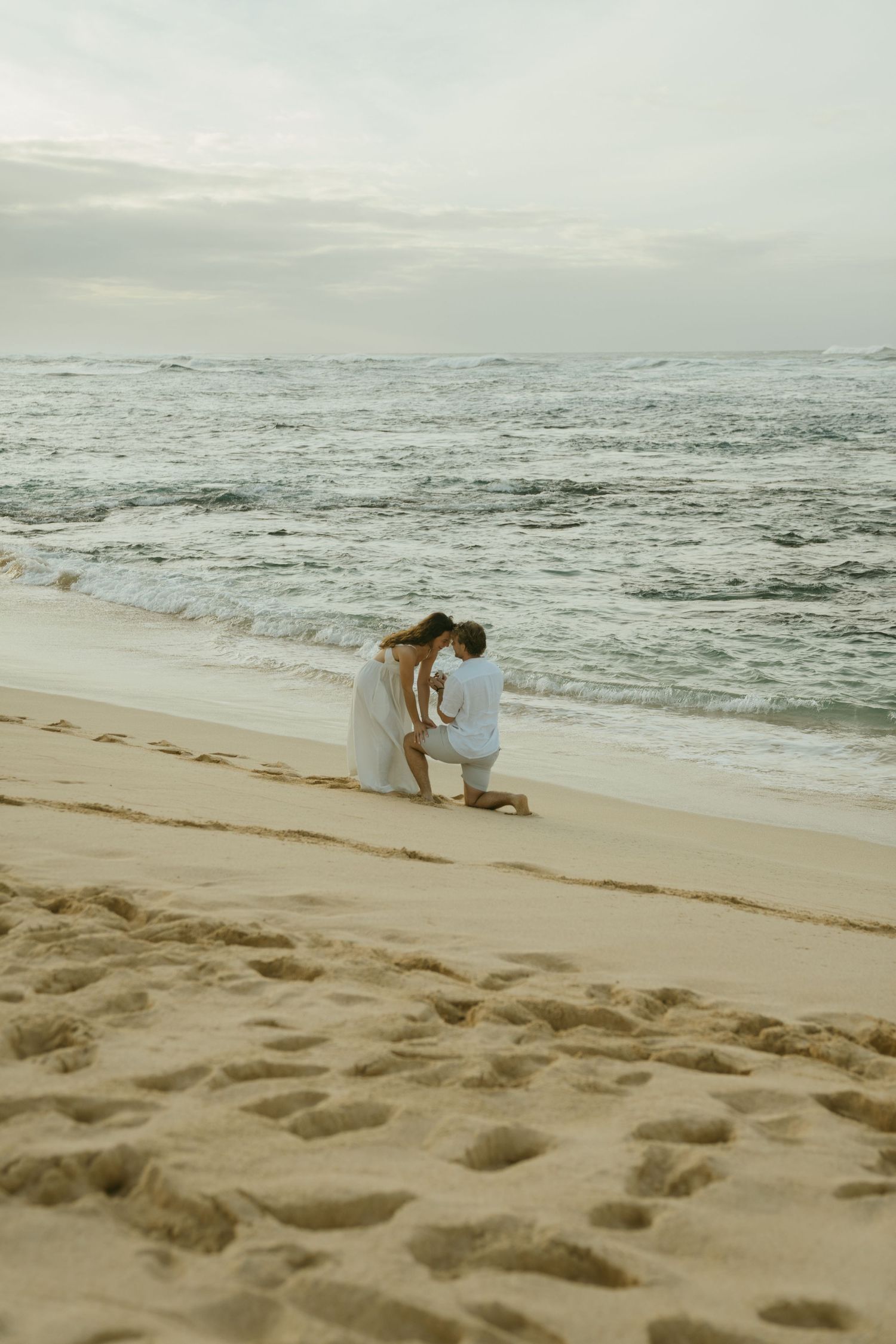 Intimate beach proposal scene with waves crashing in the background at sunset.