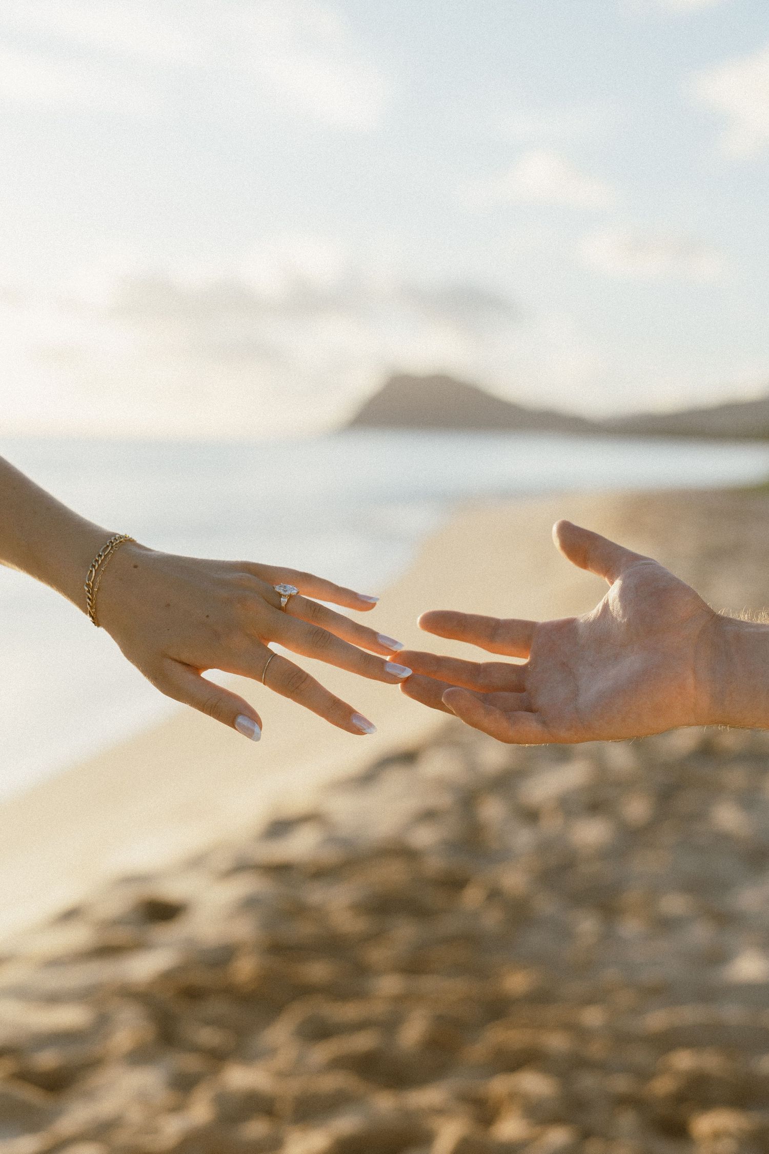Close-up of hands reaching out against a blurred beach background at sunset.