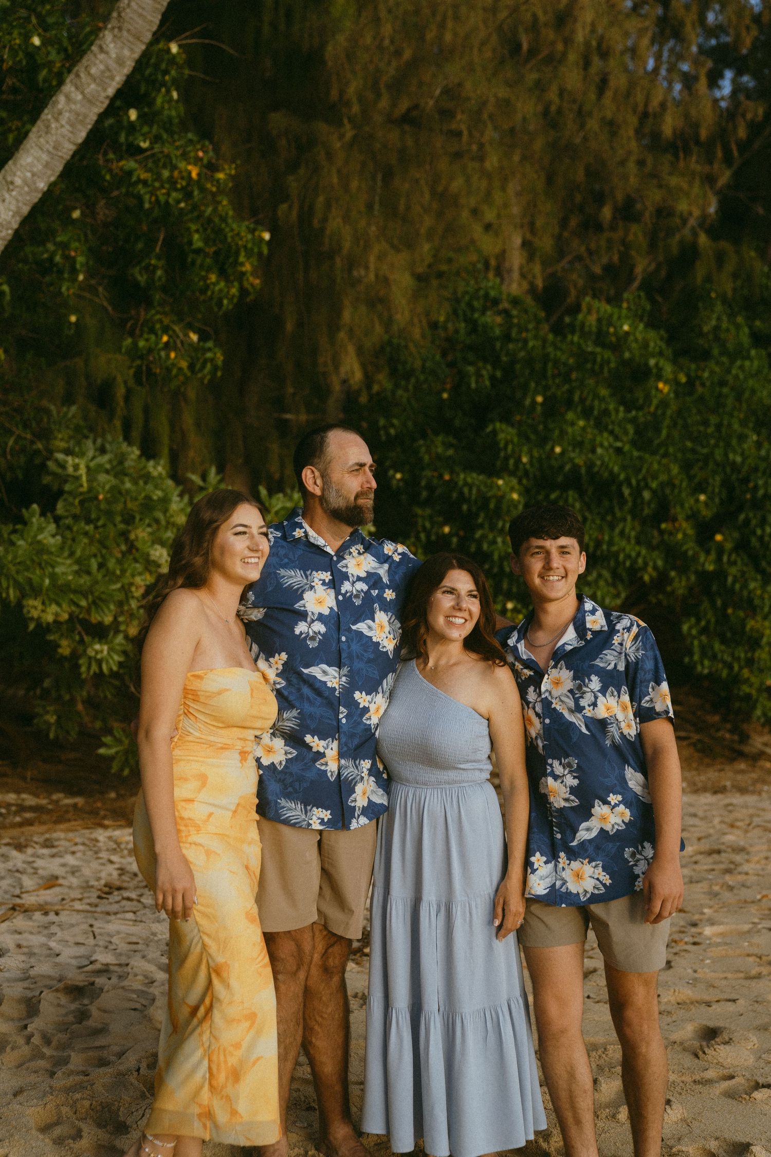 Group wearing coordinated casual outfits poses together on beach near trees.