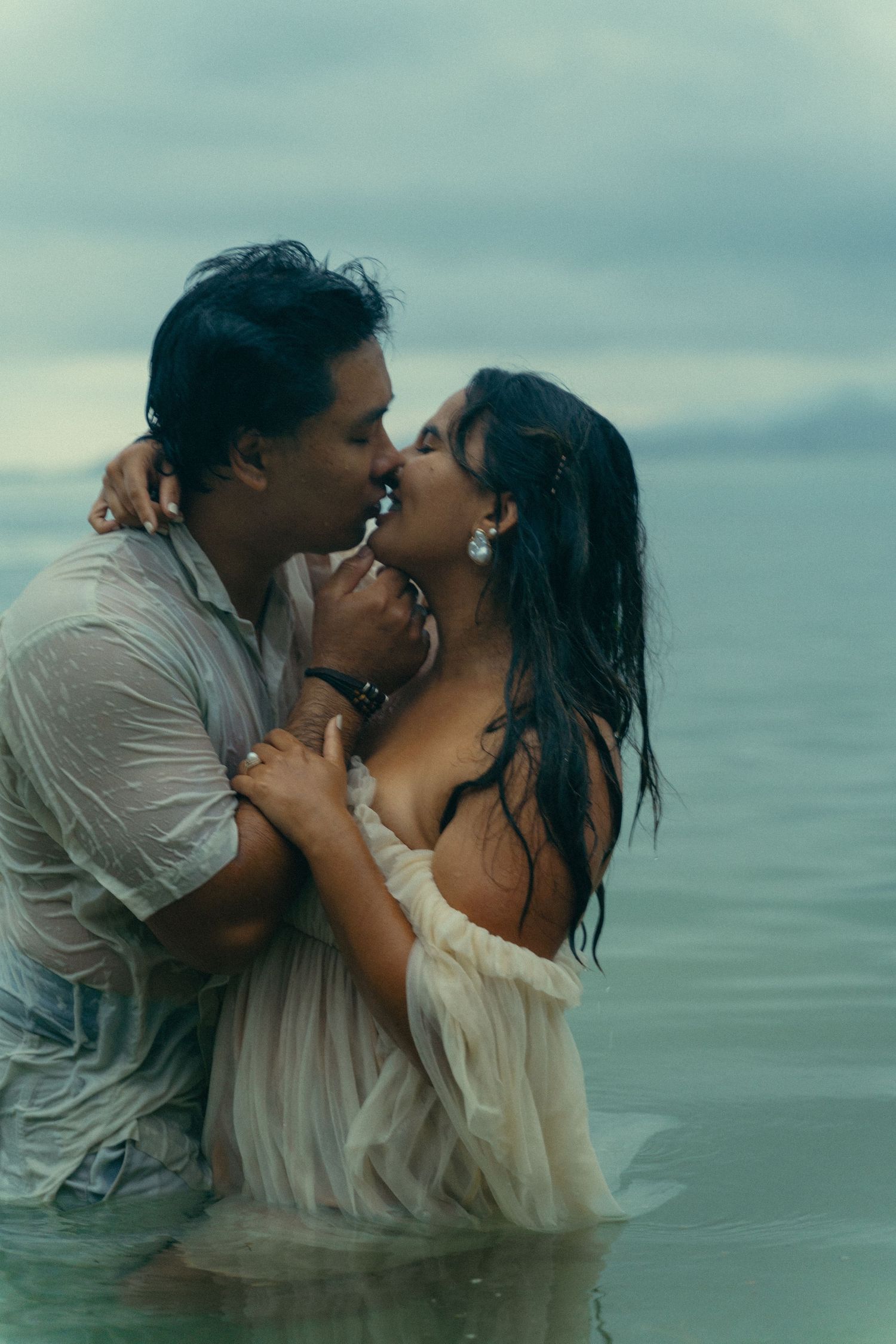 A couple shares an intimate moment while standing in ocean waters at dusk.