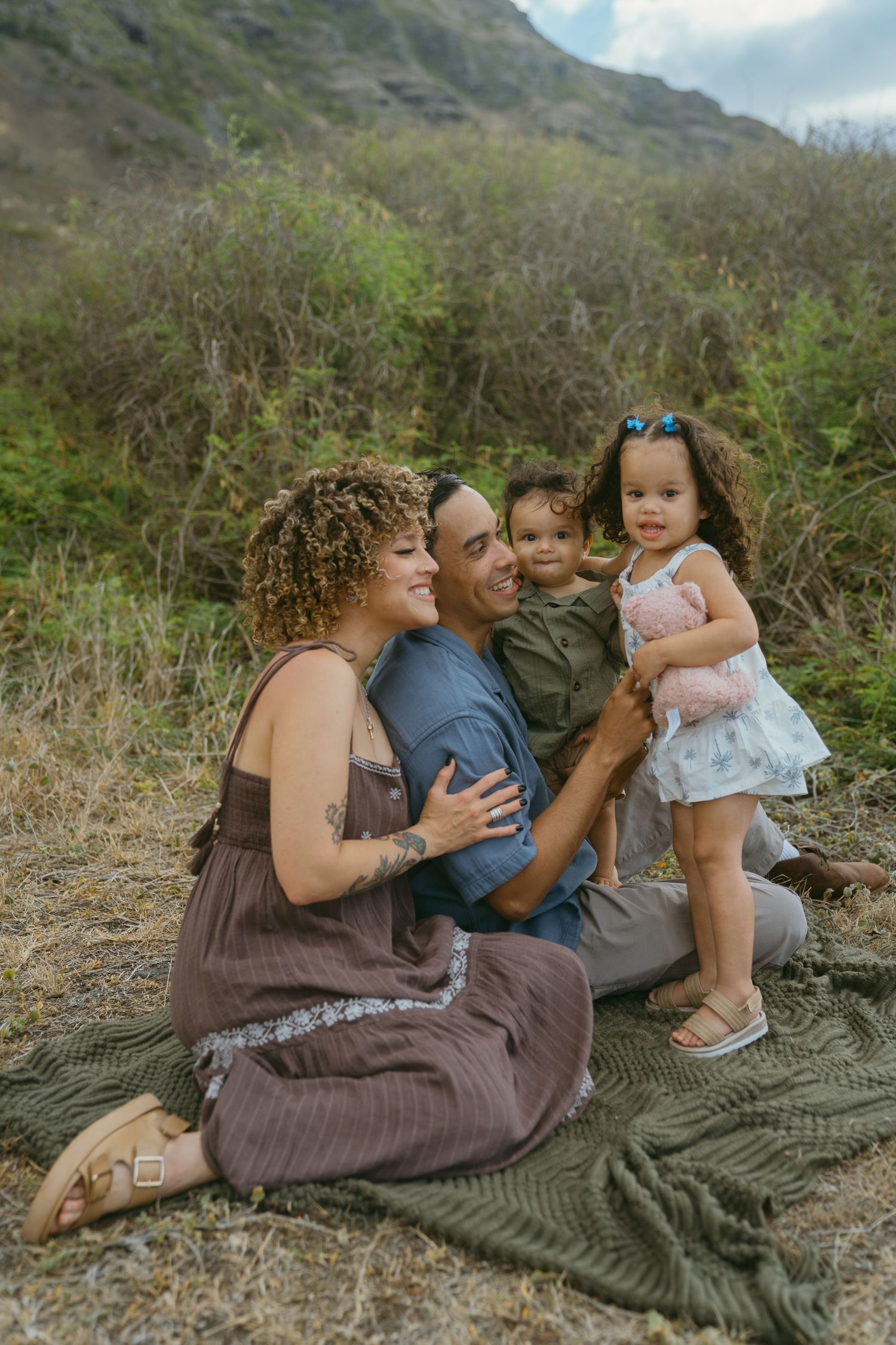 Candid family moments captured on blanket with mountain scenery in background.