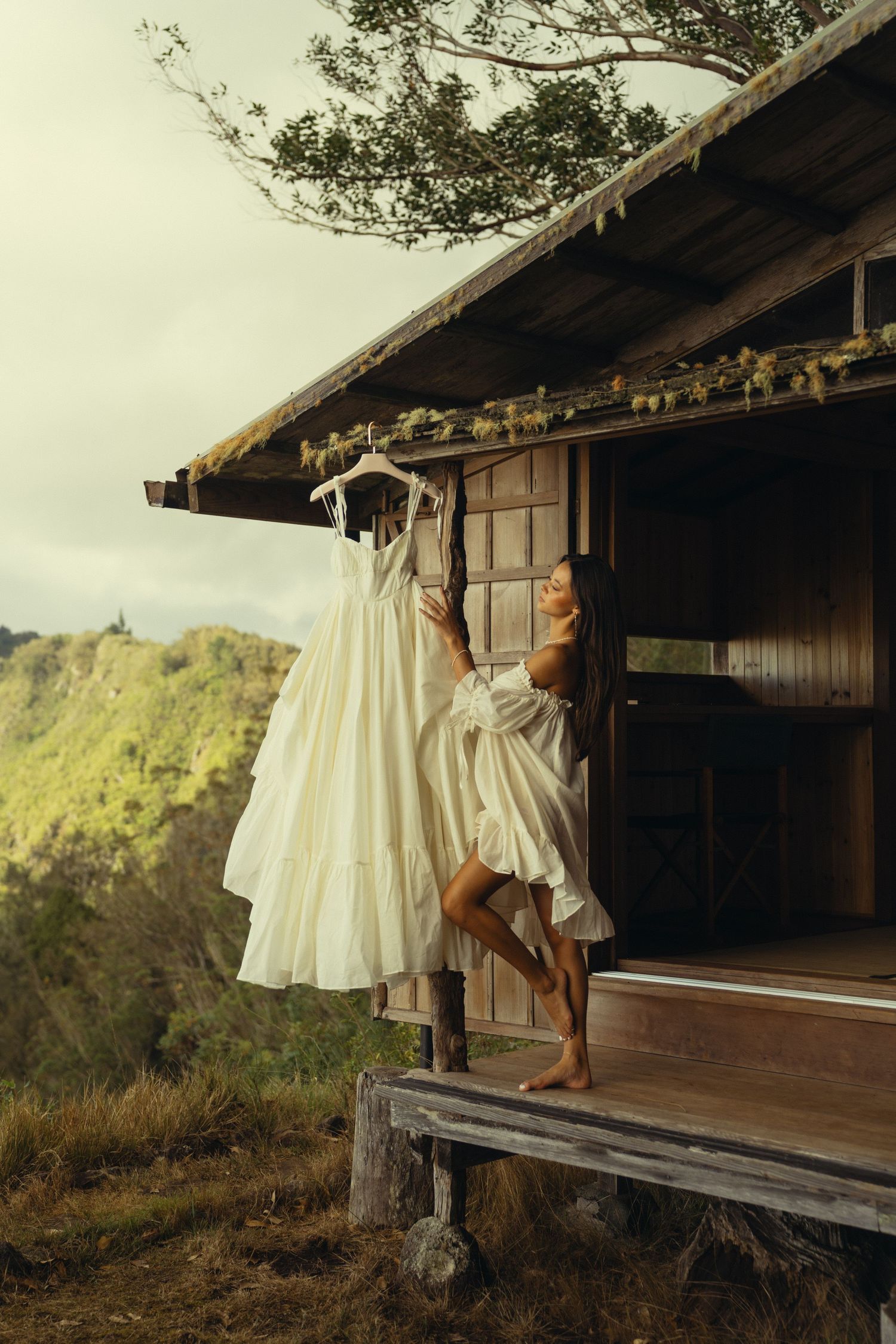 A white flowing dress moves in the breeze on a rustic wooden porch with mountains in the distance.