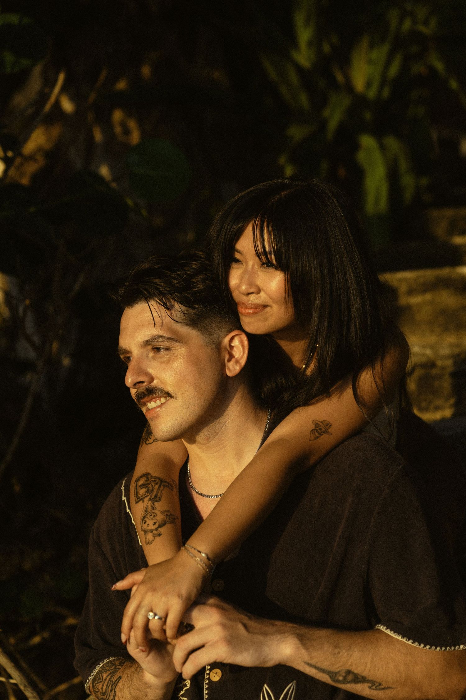 A romantic evening photoshoot with a couple in dark clothing against a shadowy natural backdrop.