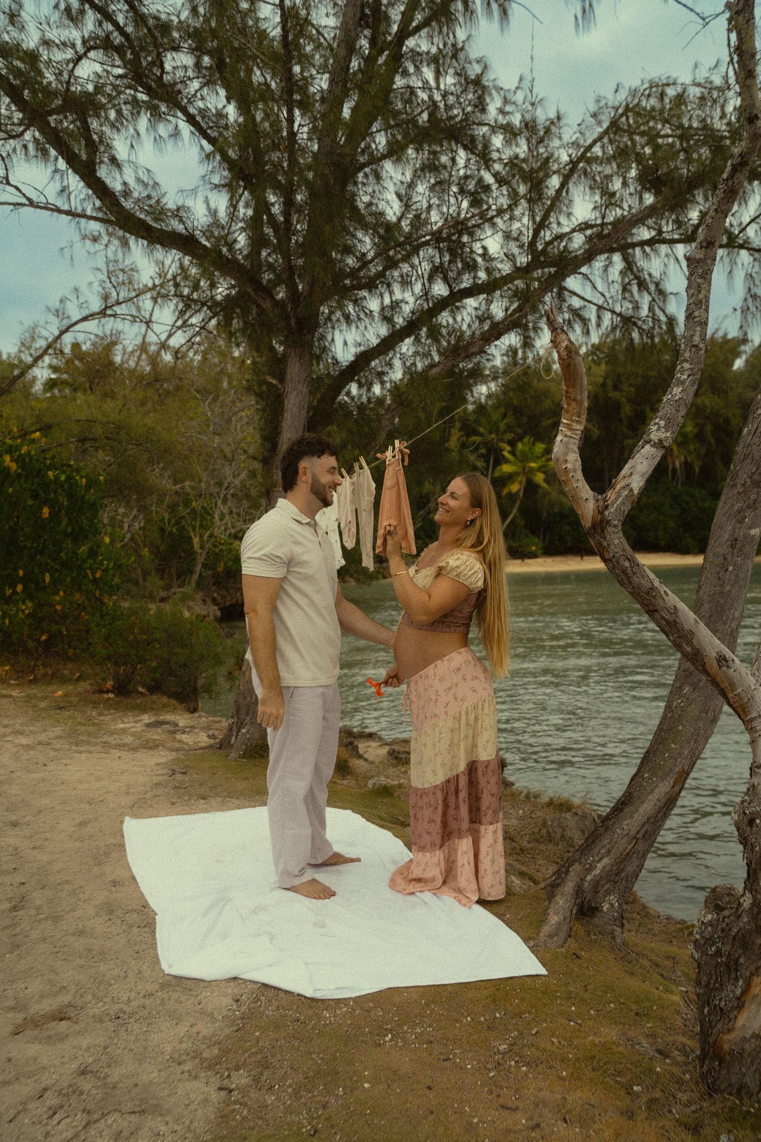 Two people share playful moments on a white blanket by the beach at sunset.