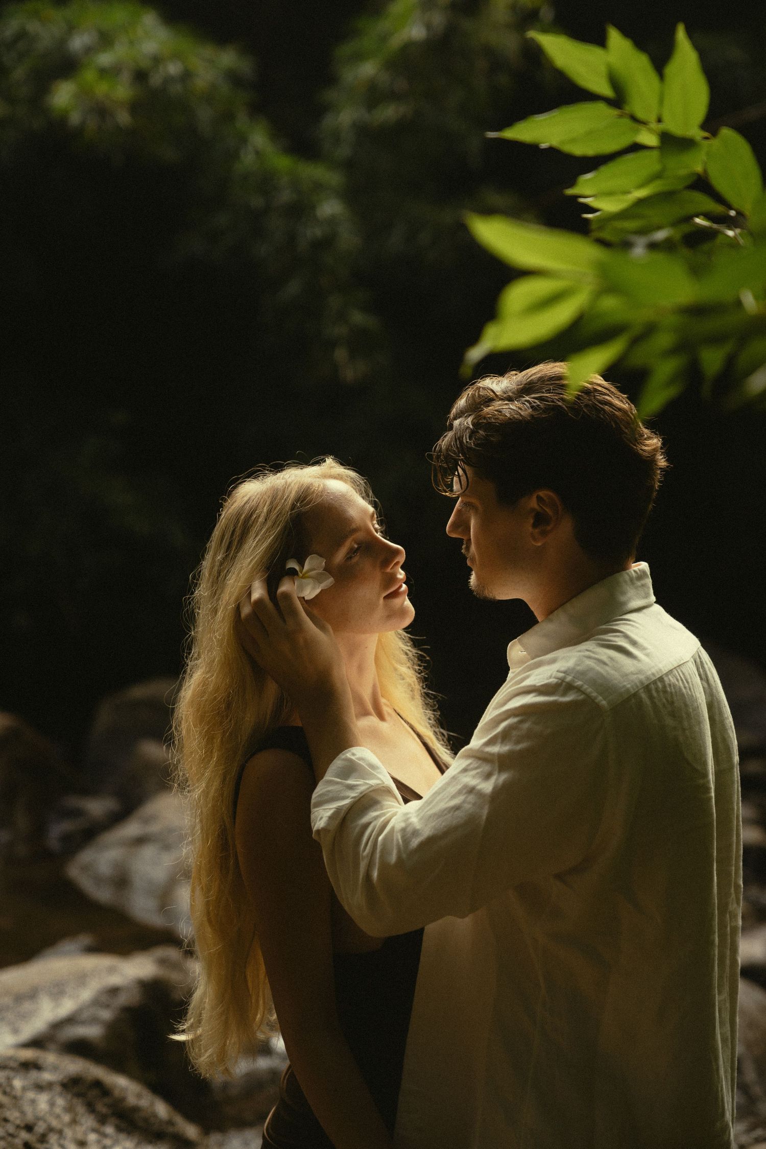 Romantic couple's portrait in a sunlit forest with ethereal golden lighting.