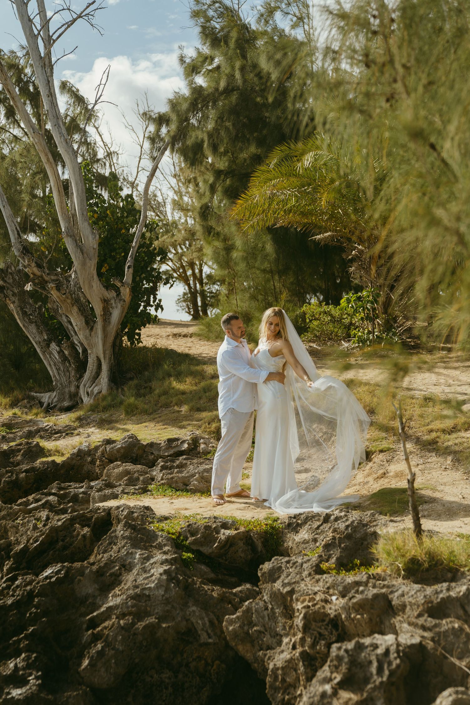 A romantic photoshoot on rocky coastal terrain with ocean views in the background.