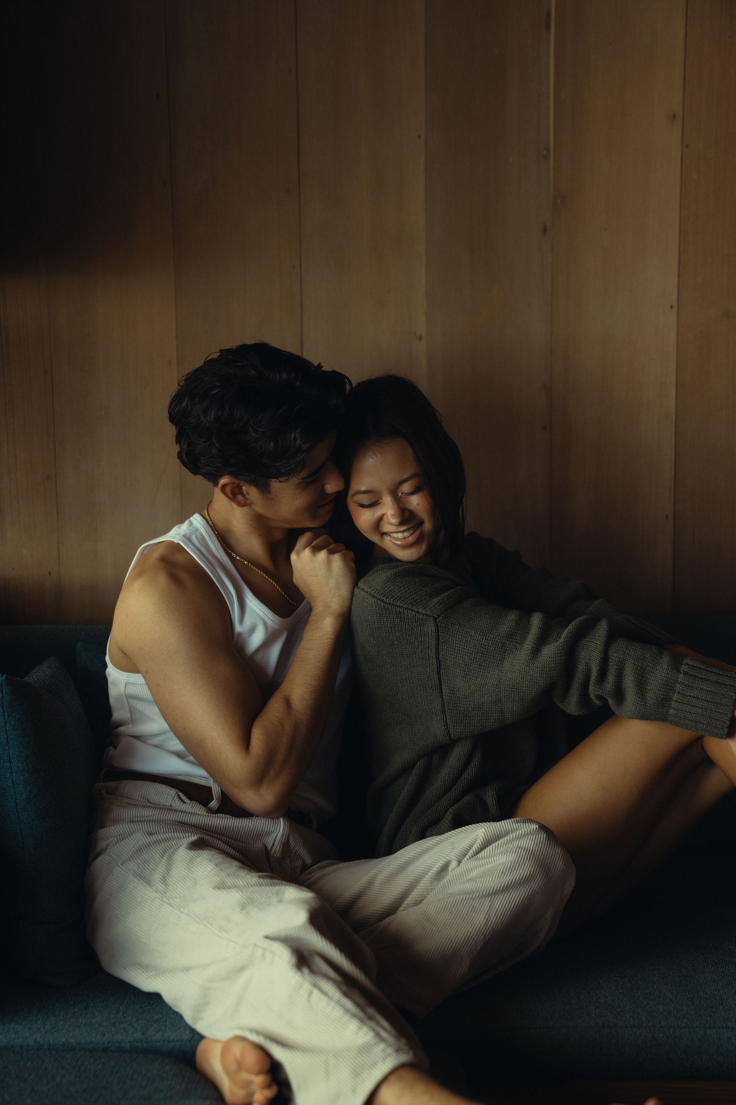 Intimate couple sharing tender moment on blue couch in warm lighting.