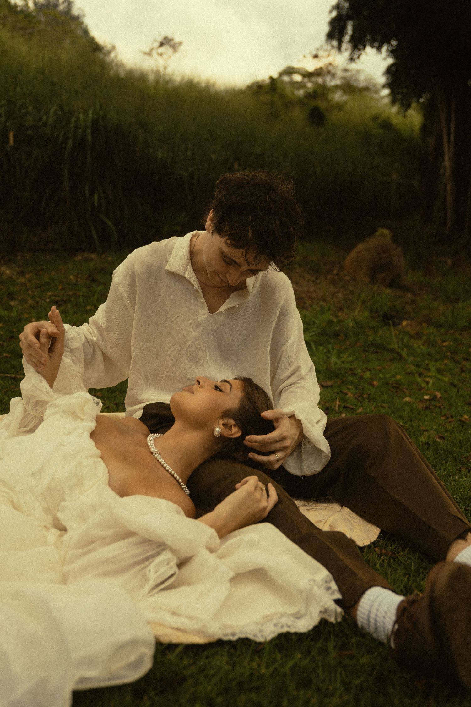 A romantic vintage-styled couple shares an intimate moment on grass during golden hour.