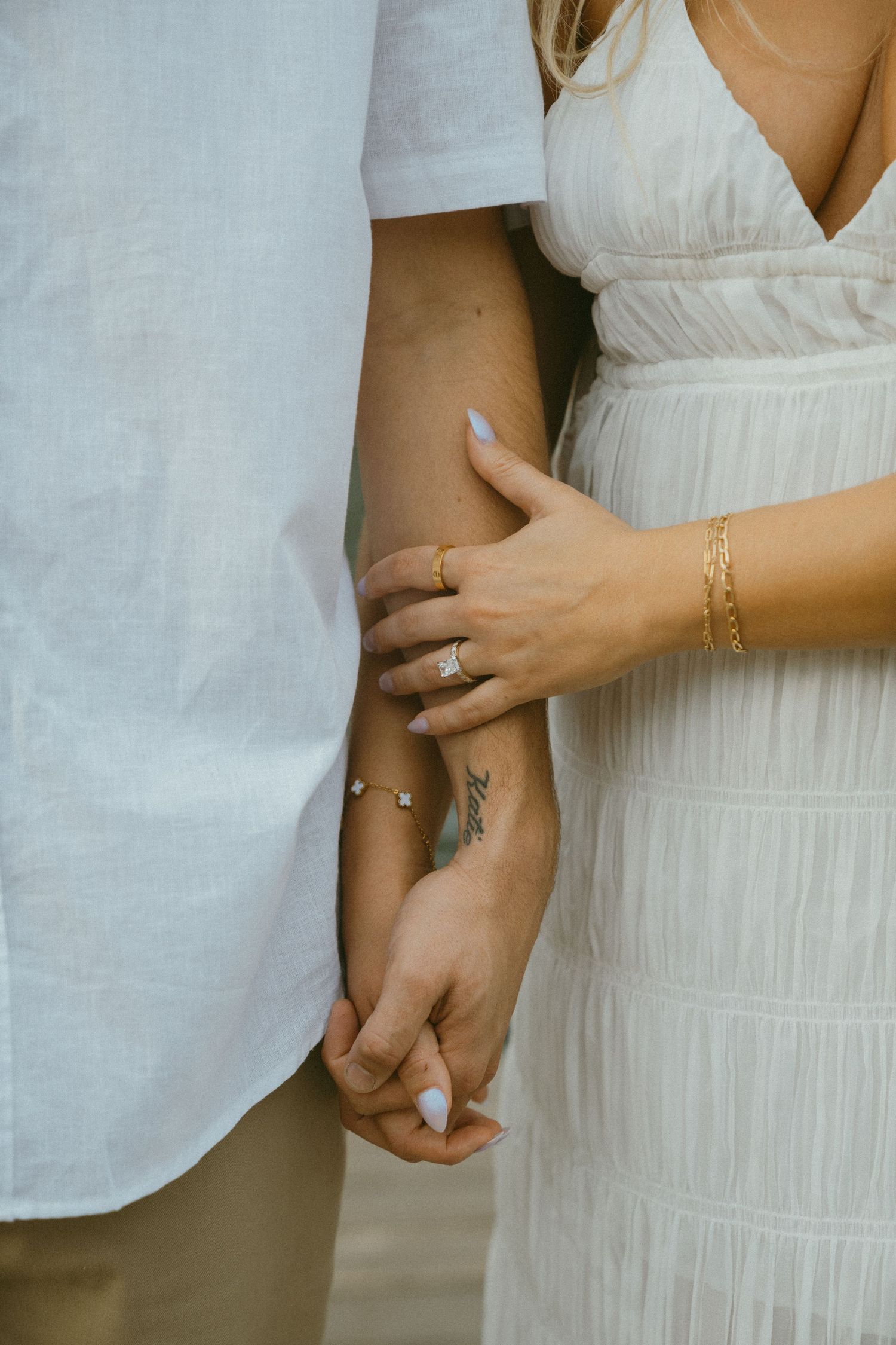 Close-up of hands embracing while wearing white clothing and delicate jewelry.