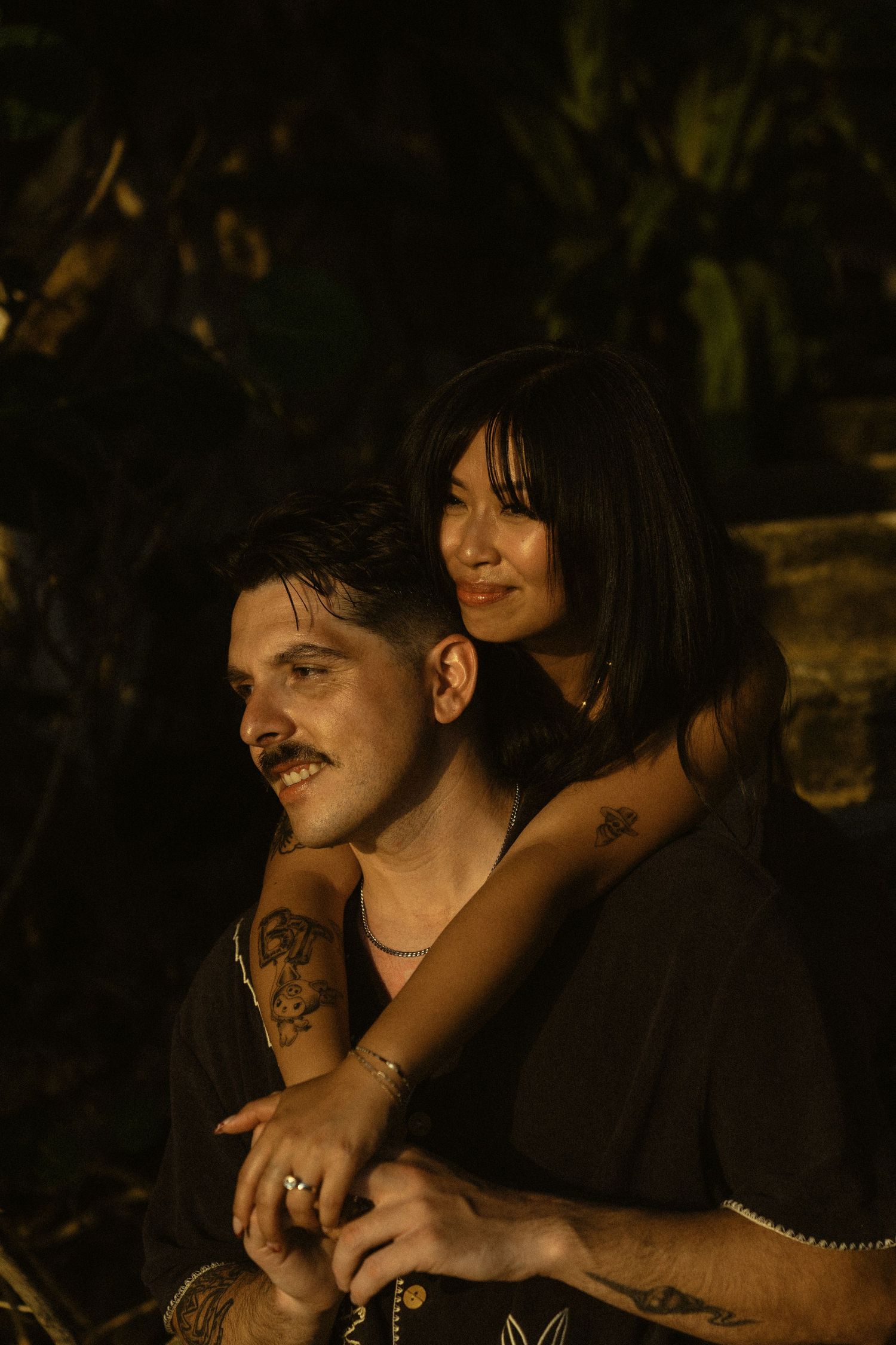 A couple shares intimate moments in a dark, moody setting with natural lighting.