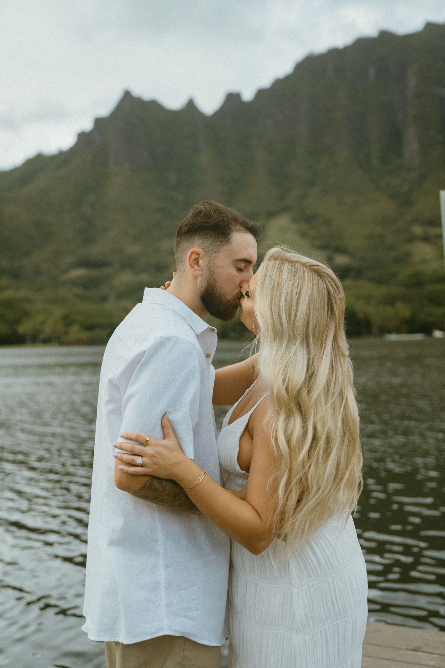 Romantic couple embracing by a lake with mountains in the background.