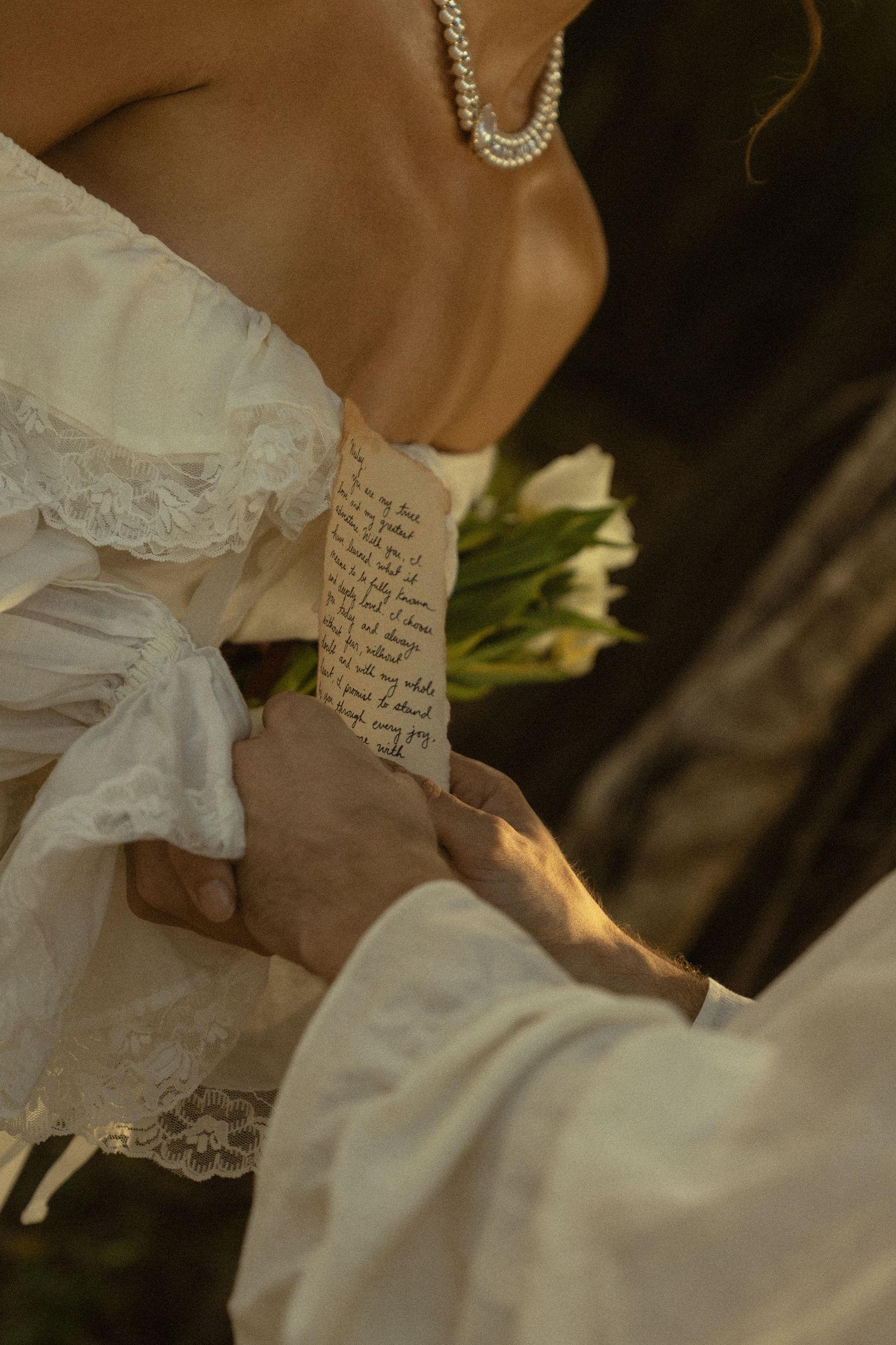 Close-up of hands holding a handwritten note with white lace and pearls in view.