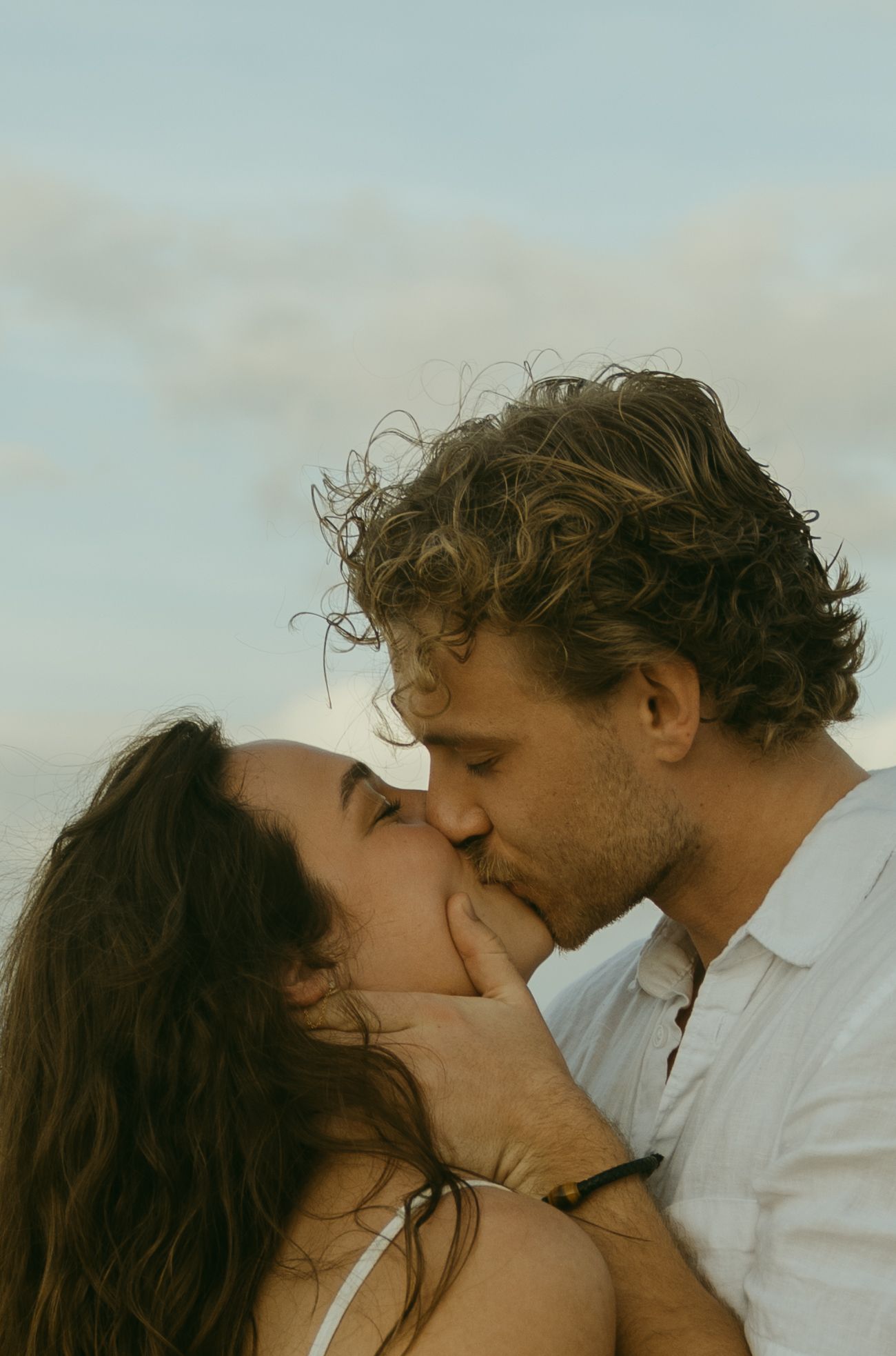 Romantic couple sharing intimate kisses against a cloudy sky in a series of connected photos.