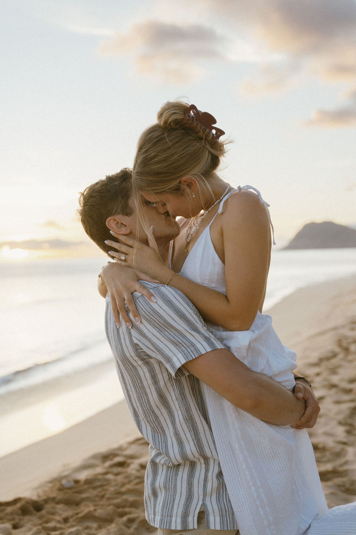 A tender embrace between two people on a sandy beach at sunset.
