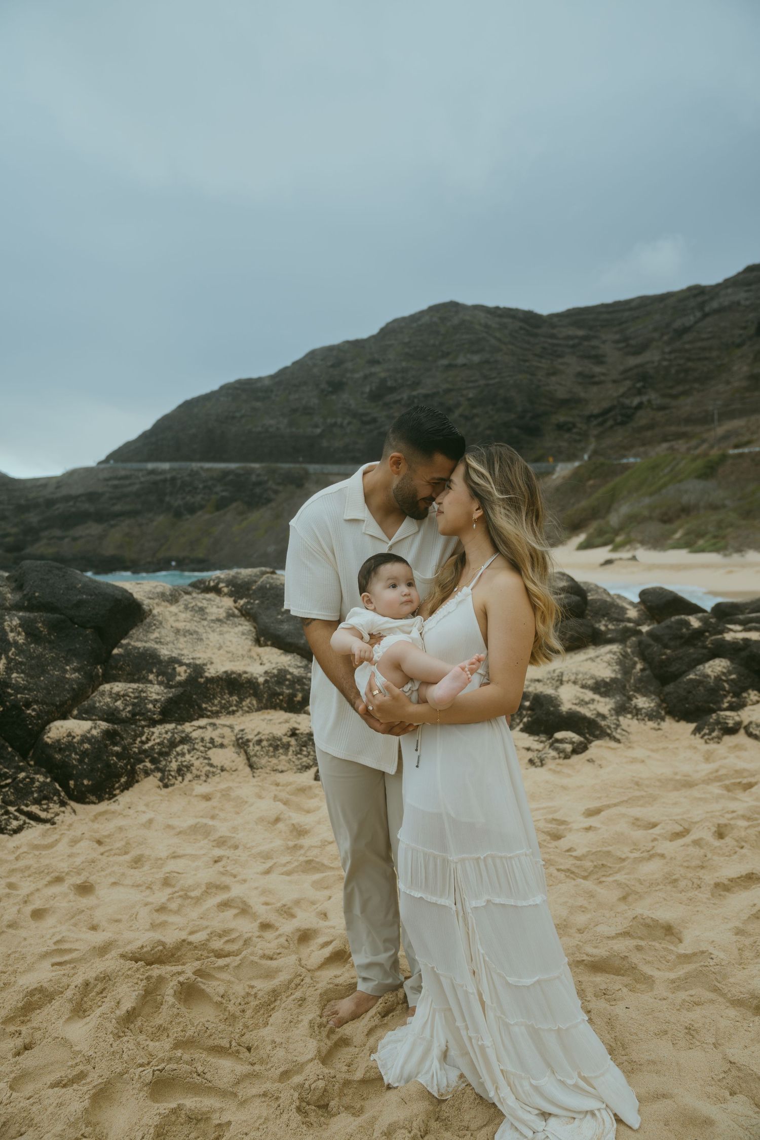Family photo session on a scenic beach with mountains and dramatic clouds in the background.