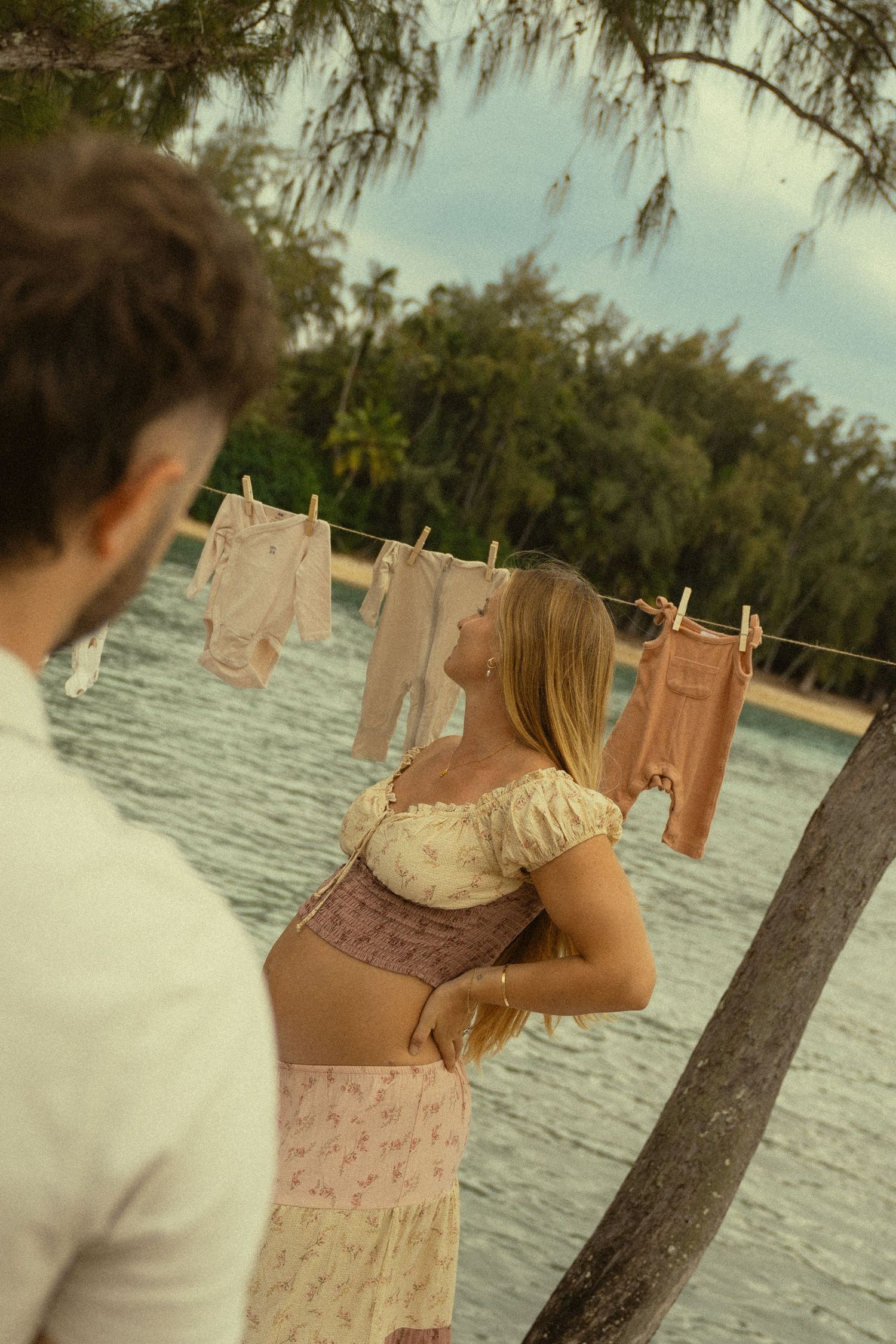 Vintage-style clothing hangs on a clothesline near the ocean with trees in the background.