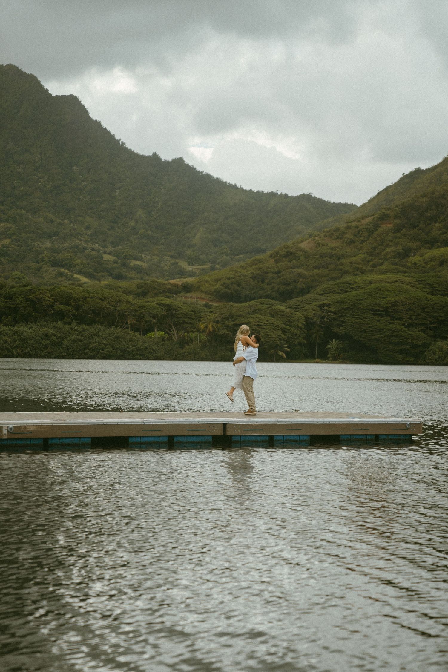 A peaceful mountain lake scene with a wooden pier stretching across rippling waters.