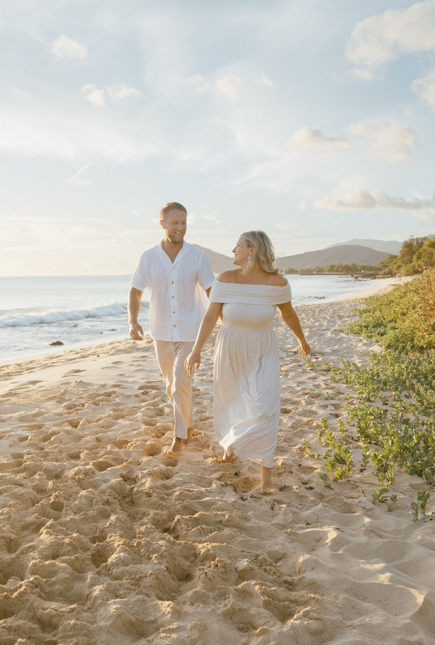 Two people in white clothing walking along a sandy beach at golden hour.