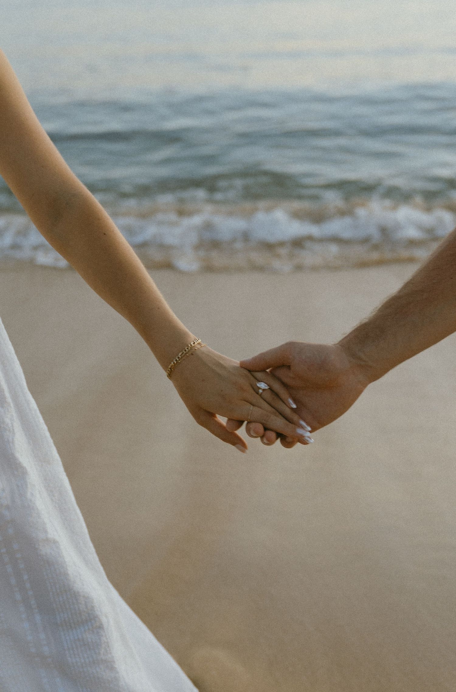 Close-up of hands holding together against an ocean backdrop.