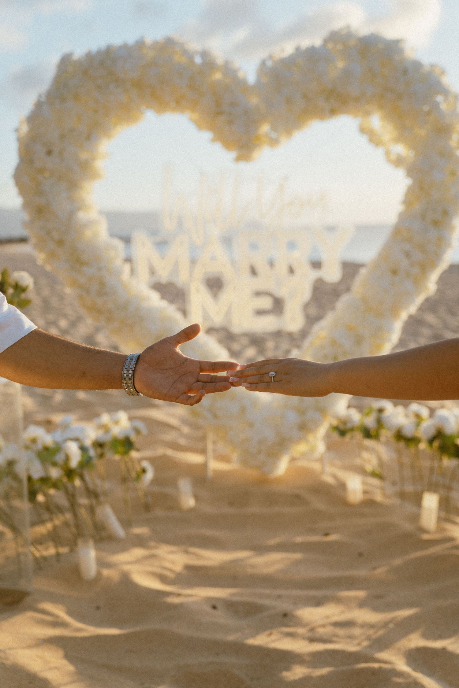 White floral arches line a sandy beach path at sunset creating a romantic wedding aisle.