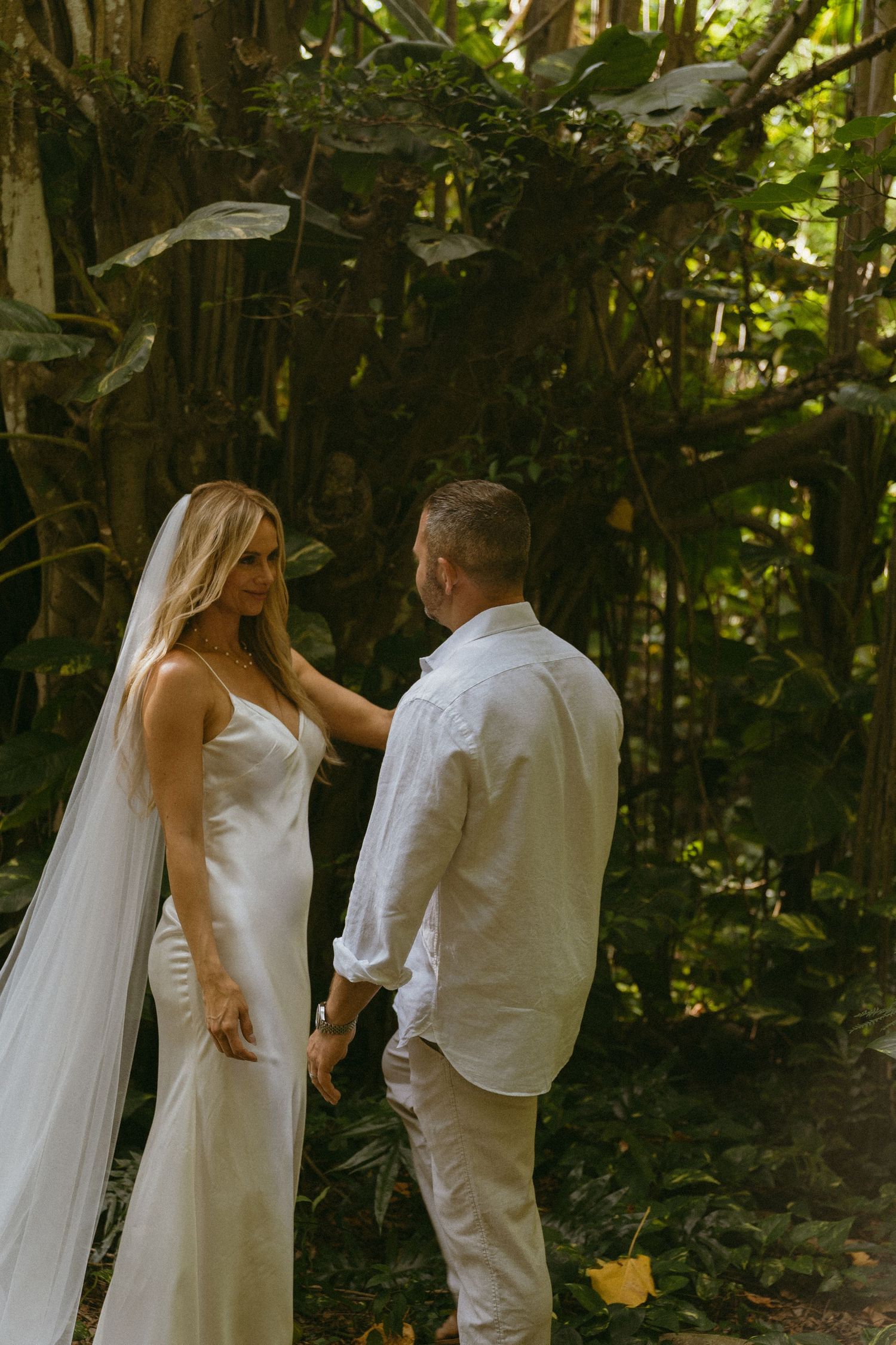 A wedding couple shares an intimate moment in a lush forest setting.