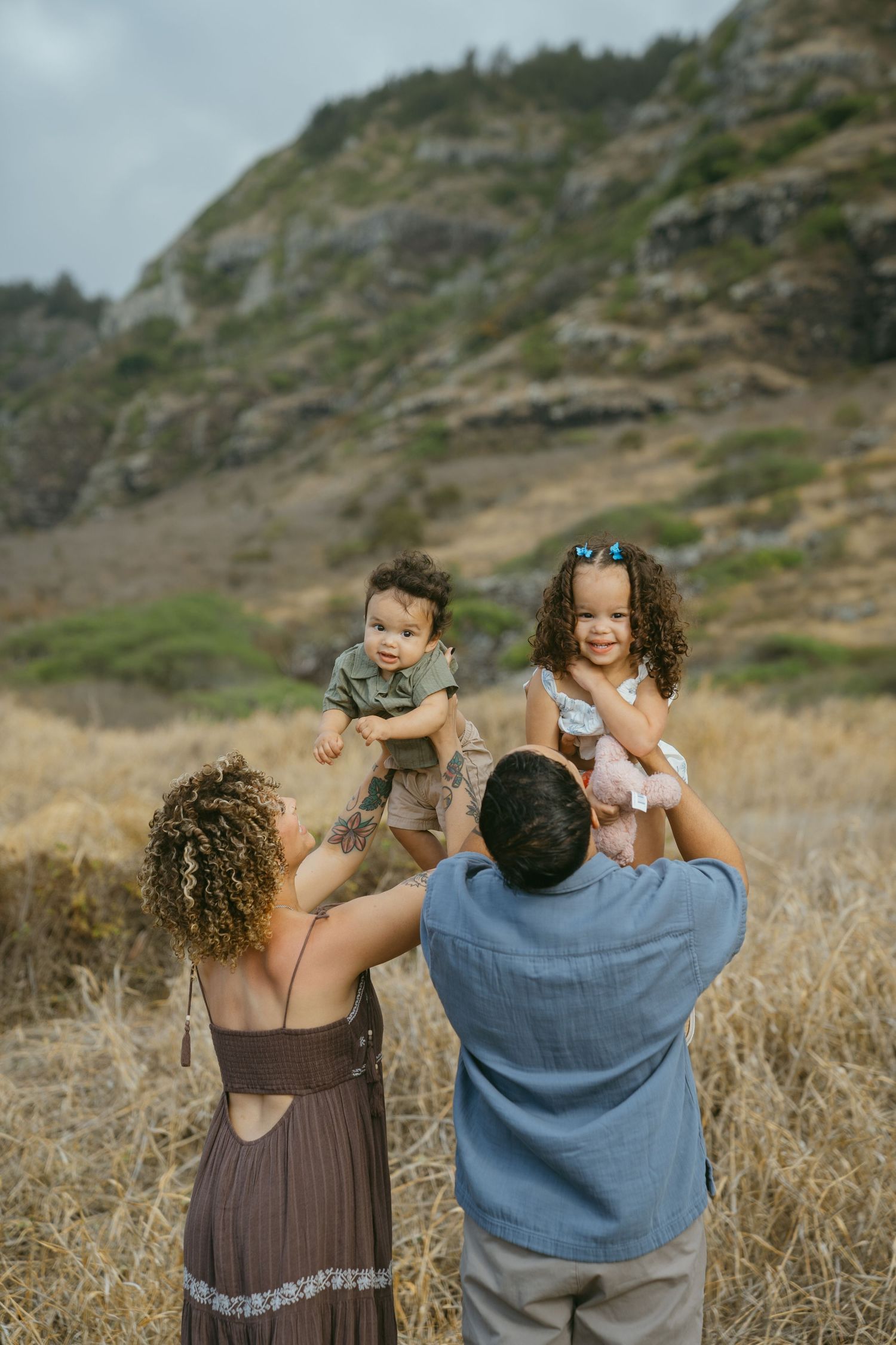 Family members pose together on a grassy hillside during an outdoor photo session.