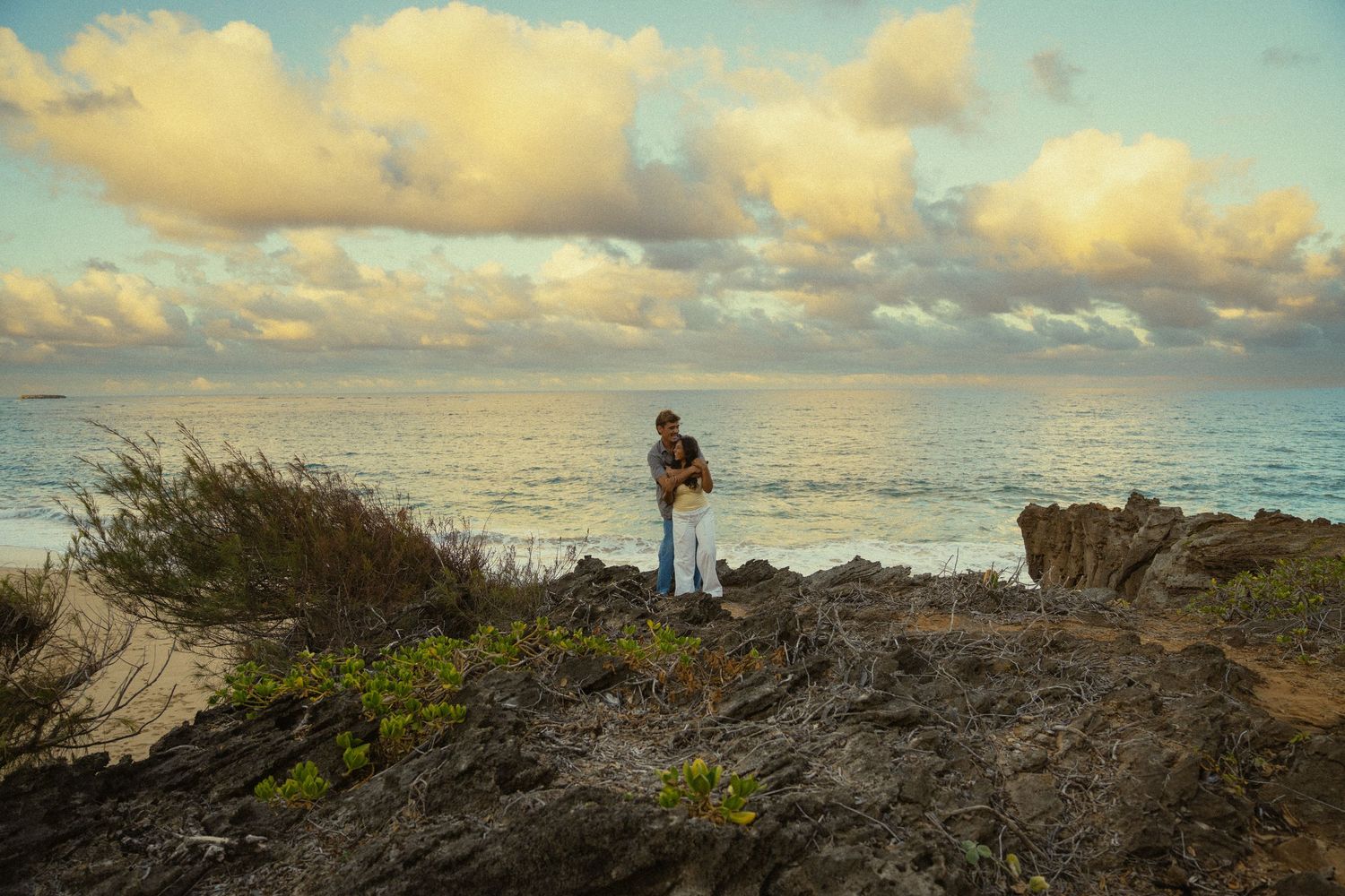 Scenic Hawaiian beach landscape with rocky coastline and dramatic clouds during golden hour.