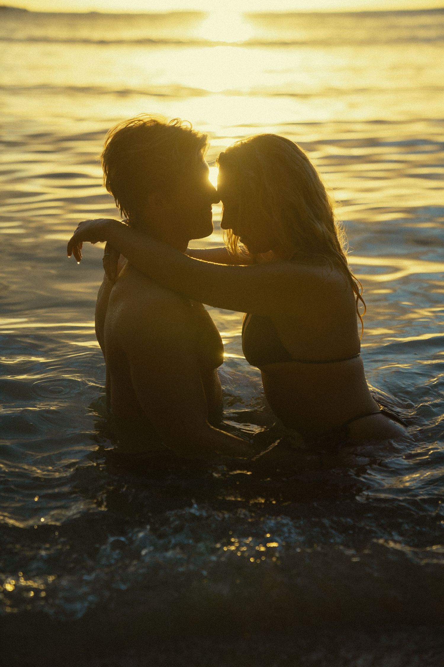 A silhouetted couple shares an intimate moment in the ocean water during sunset.
