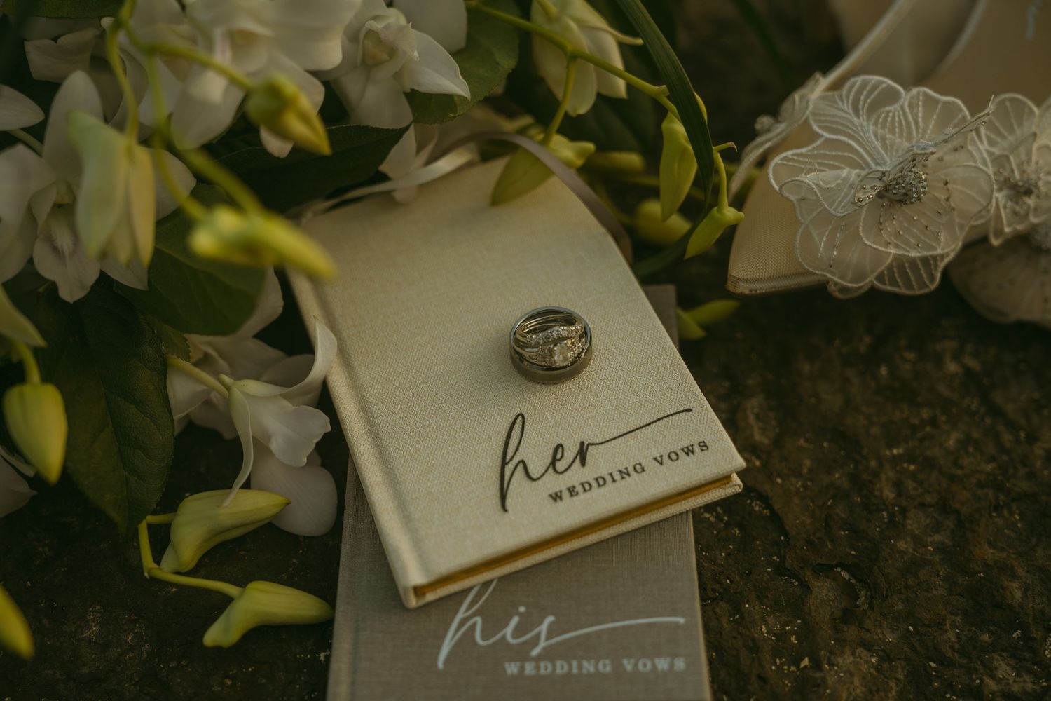 Wedding rings and vows book displayed among white flowers and delicate lace.