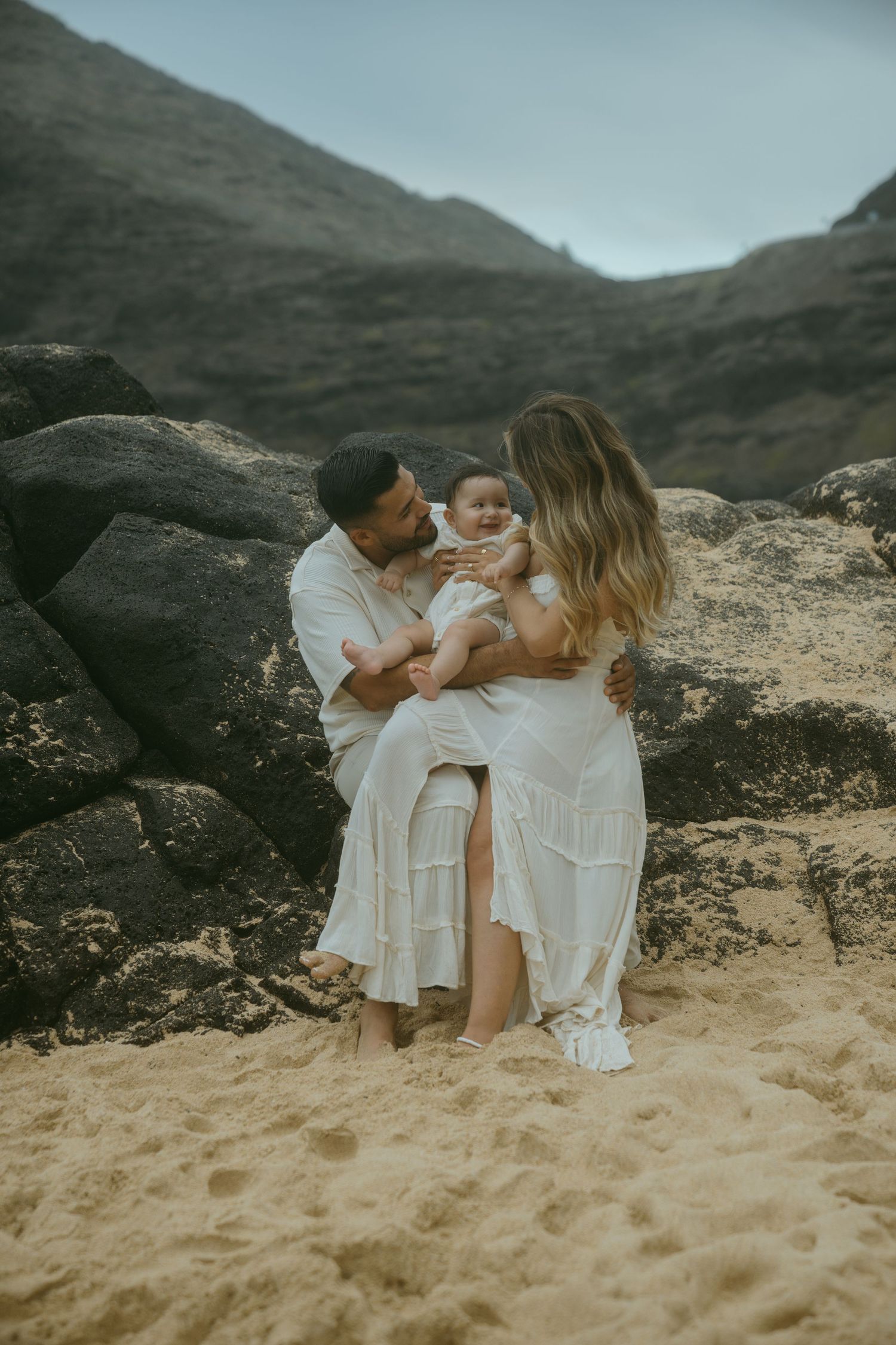 Intimate family portraits on a secluded beach with volcanic rocks and mountains.