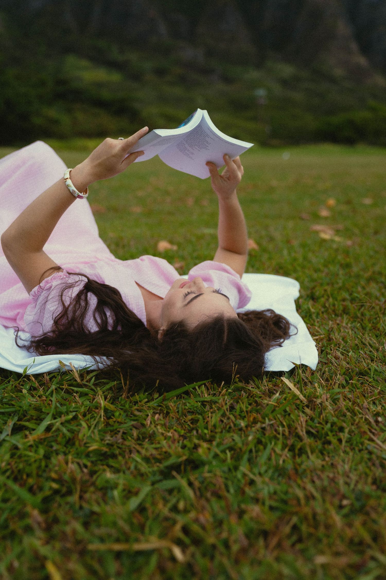 Person in pink dress lies peacefully on green grass during outdoor photo session.