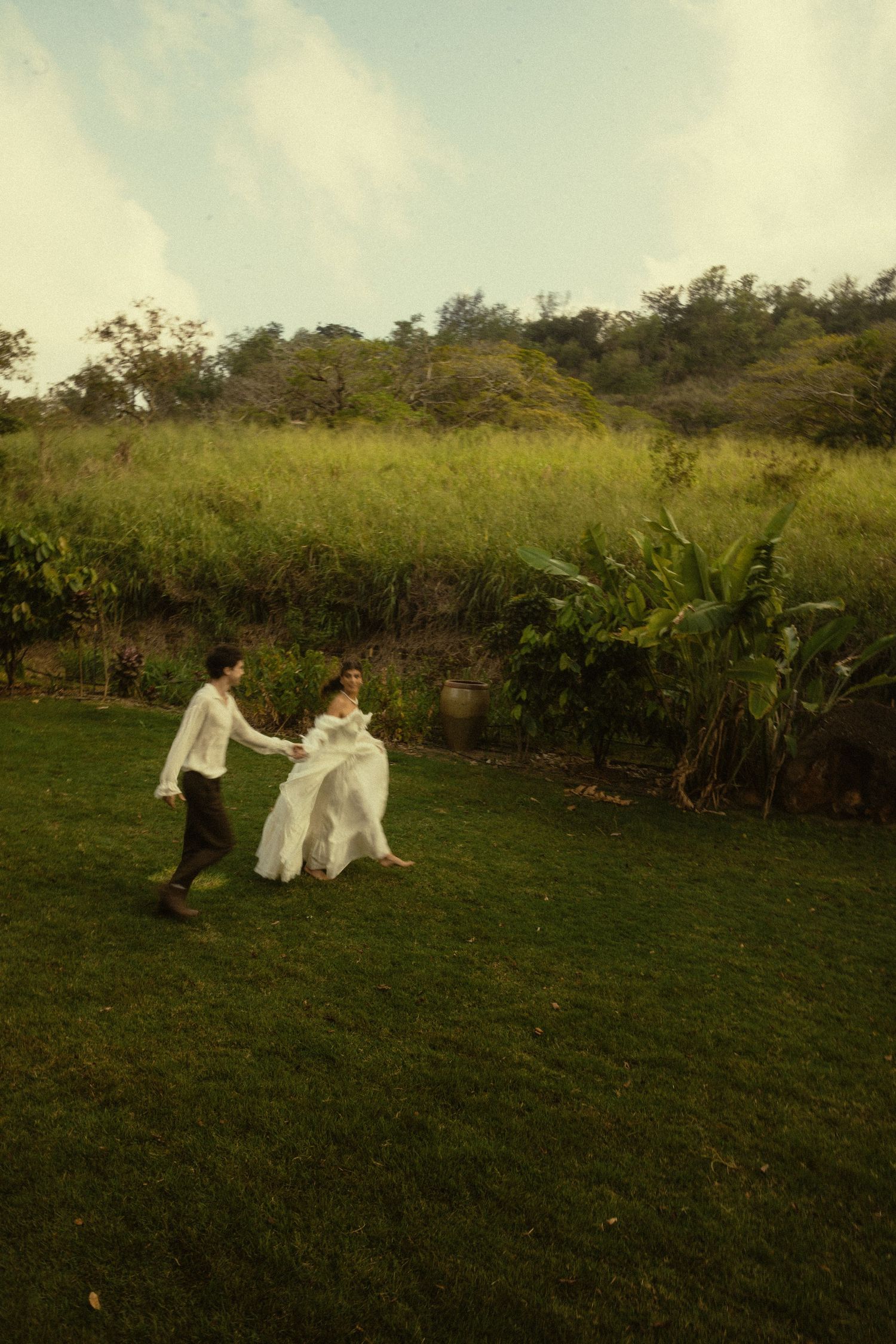 A couple dances together on a grassy hillside in vintage-inspired wedding attire.
