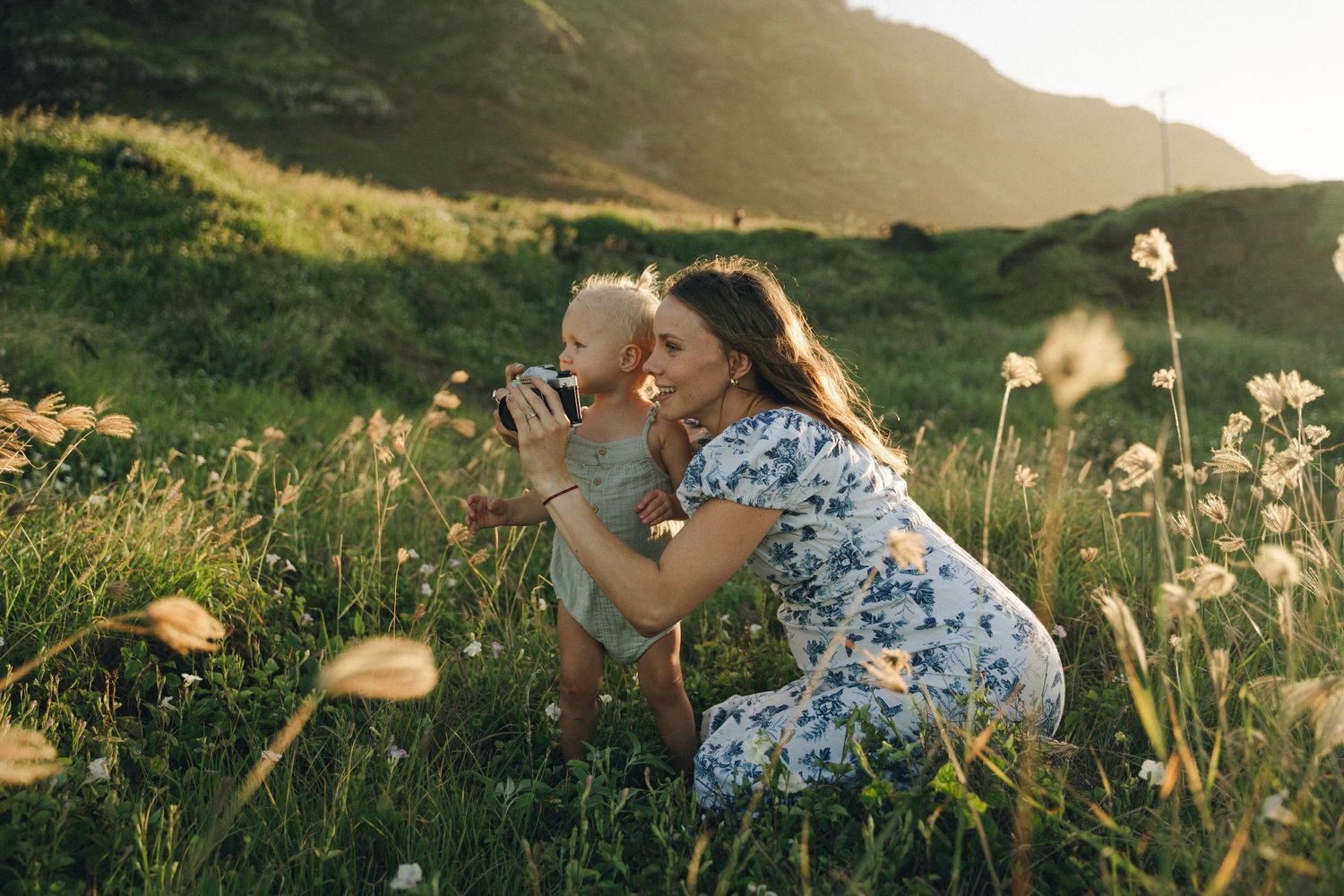 Playful family moment captured in a golden-lit field with mountains in background.