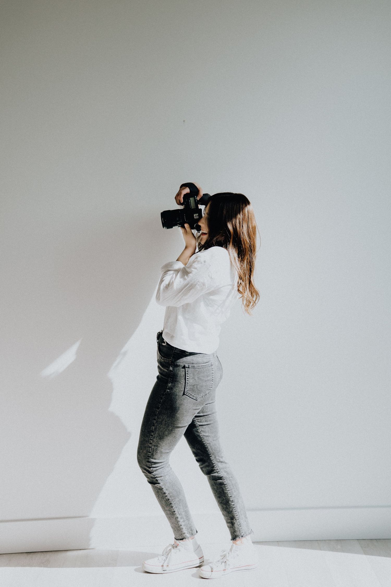 Photographer in casual attire shooting with professional camera against white background.