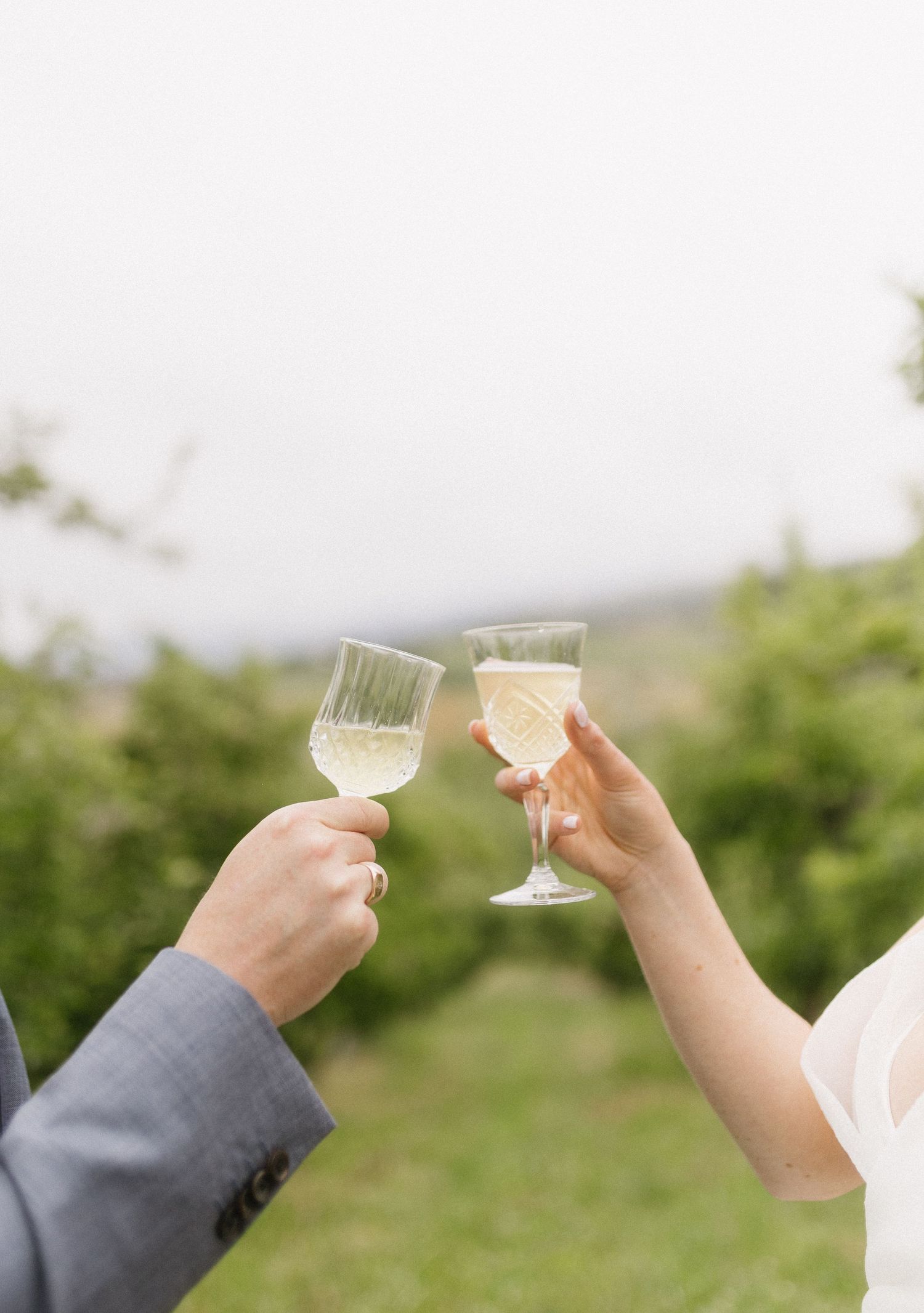 Two champagne glasses clinking in a celebratory toast against a blurred outdoor background.