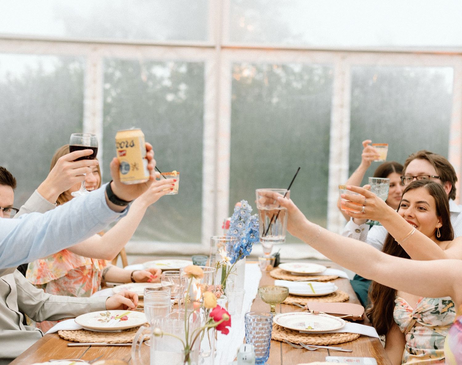 Wedding reception guests celebrating and raising glasses for a toast at long dining tables.