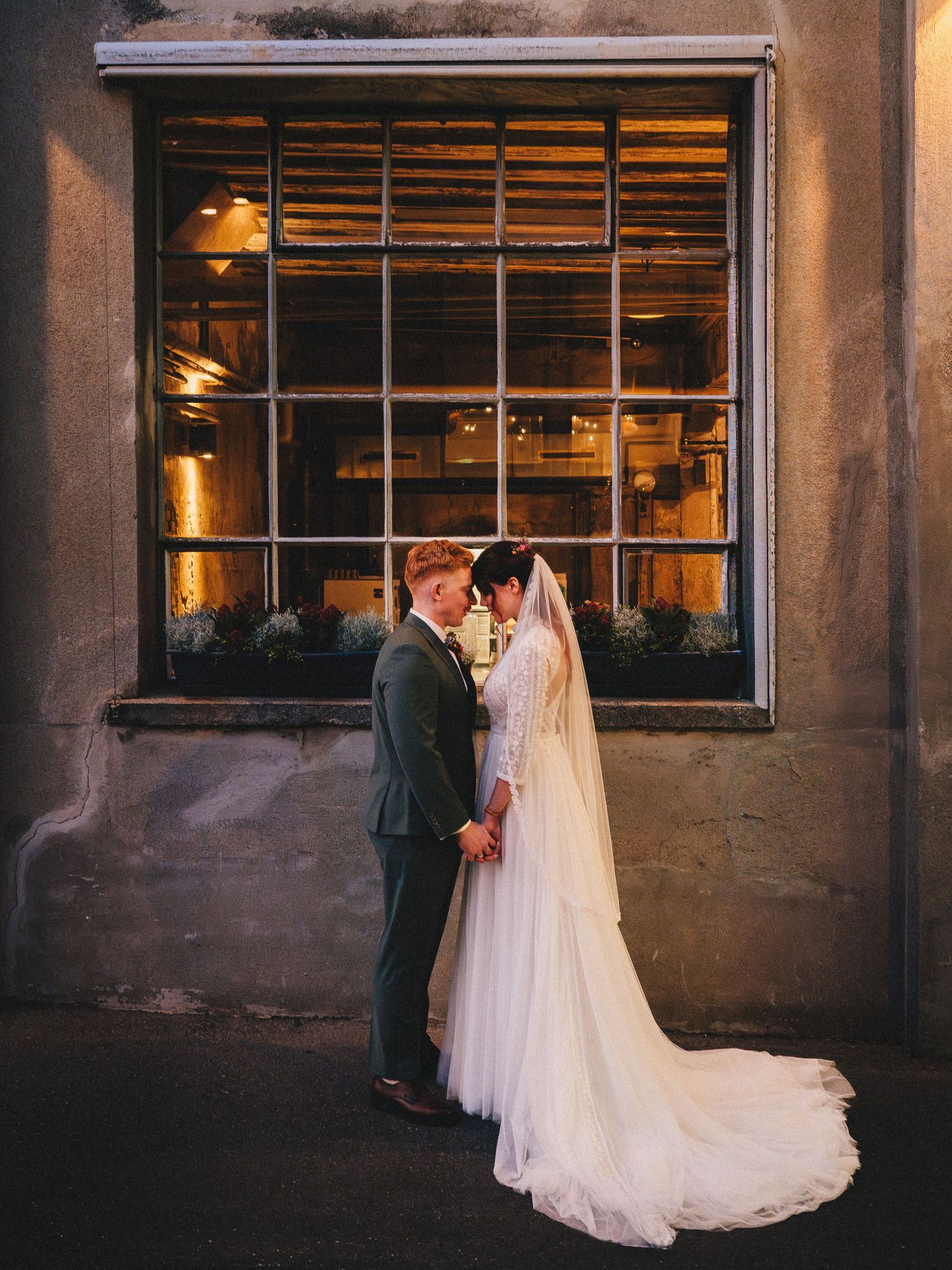 Wedding couple silhouetted against industrial windows at sunset.