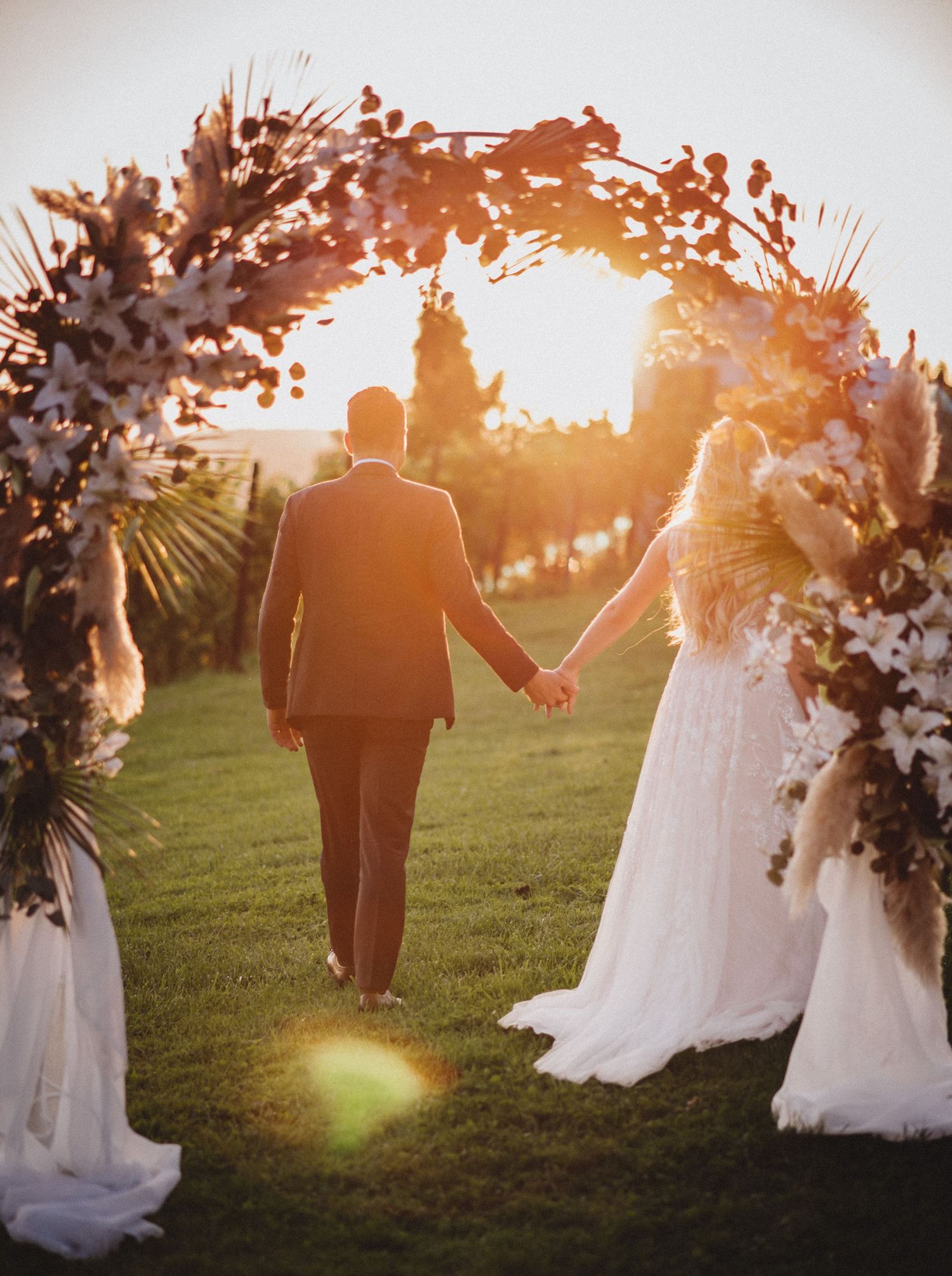 Ein Paar in Hochzeitskleidung geht während der goldenen Stunde durch einen sonnenbeschienenen Garten und bildet eine romantische Silhouette